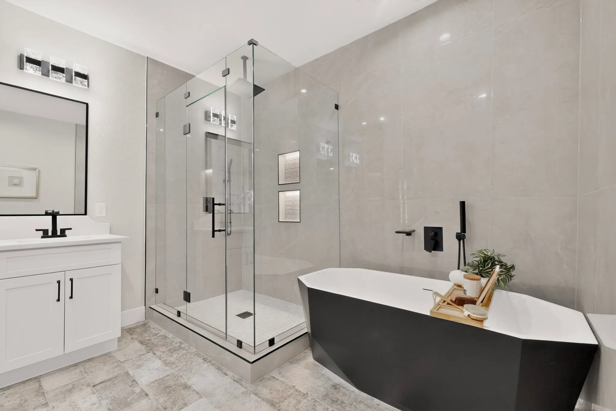 Spacious bathroom featuring a frameless glass shower enclosure, a freestanding soaking tub, a white vanity with integrated sink, and large format wall and floor tiling