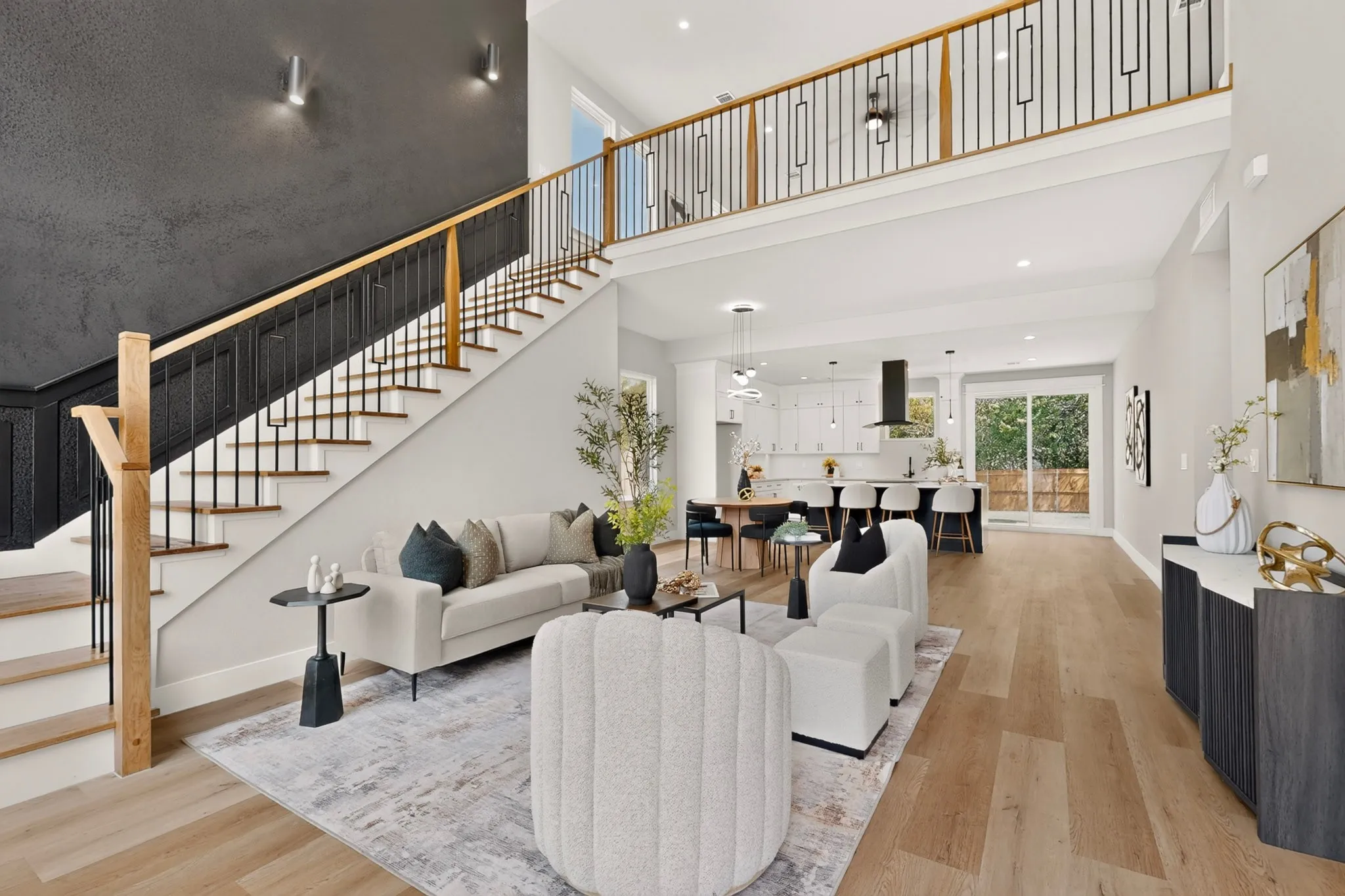 Two-story ceiling, wood-finish flooring, modern staircase with wood handrail and black balusters, open-concept layout, recessed lighting