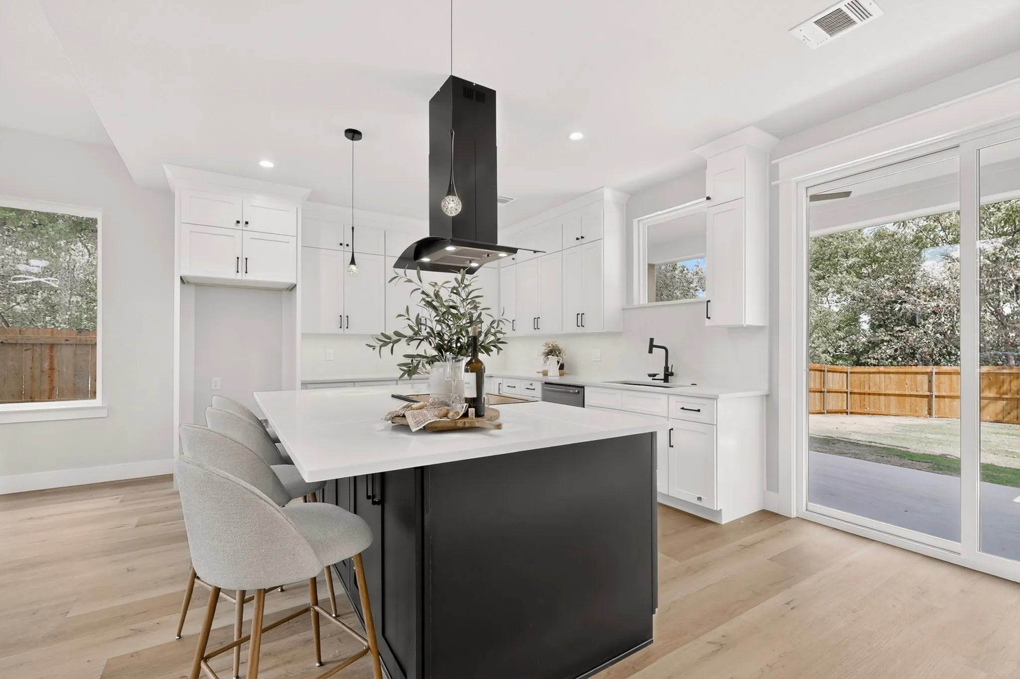 Open-concept kitchen featuring a dark-toned island with a light-toned countertop, white cabinetry, wood-finish flooring, and a sliding glass door