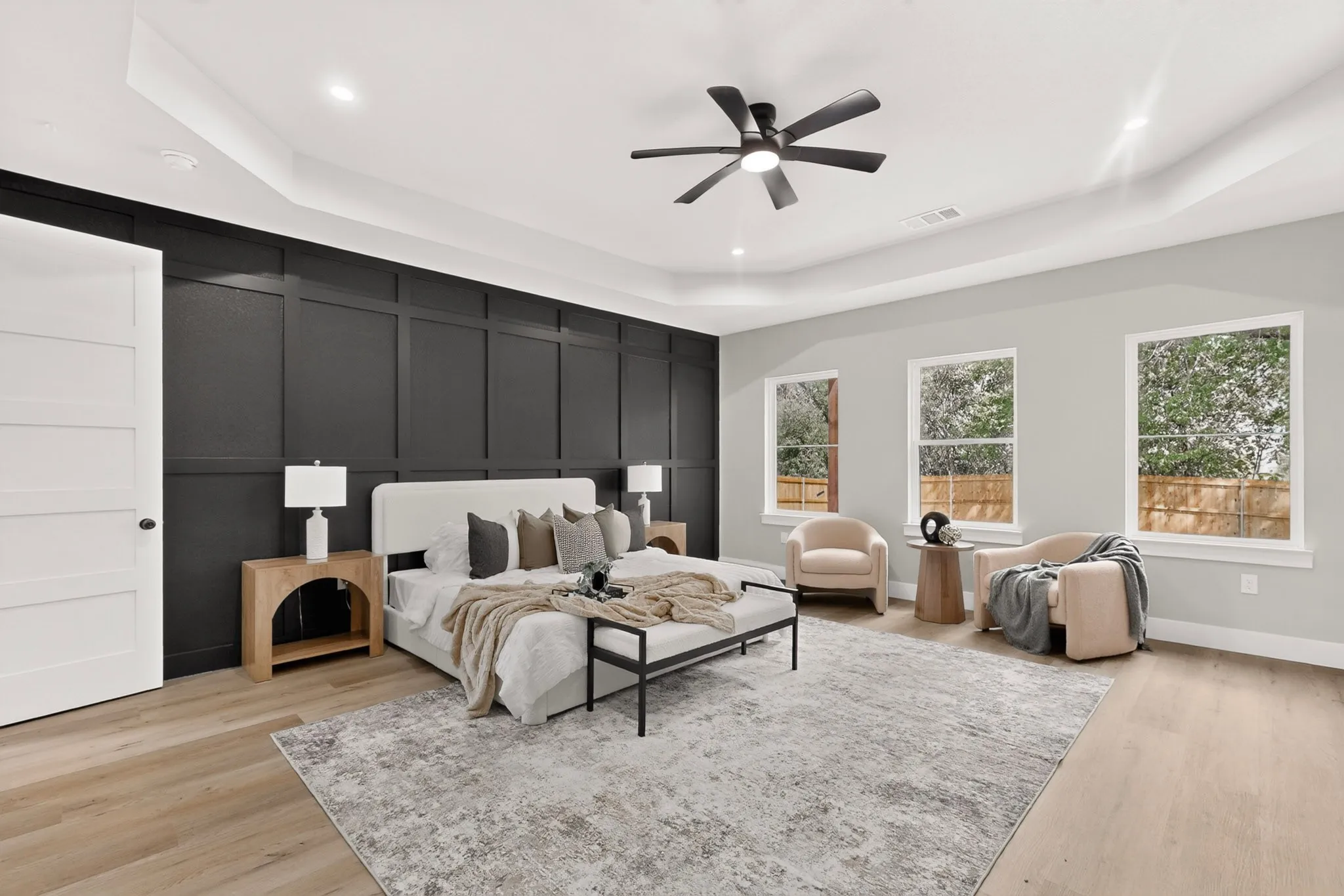 Tray ceiling with recessed lighting, black accent wall with paneling, wood-finish flooring, contemporary ceiling fan, and three large windows