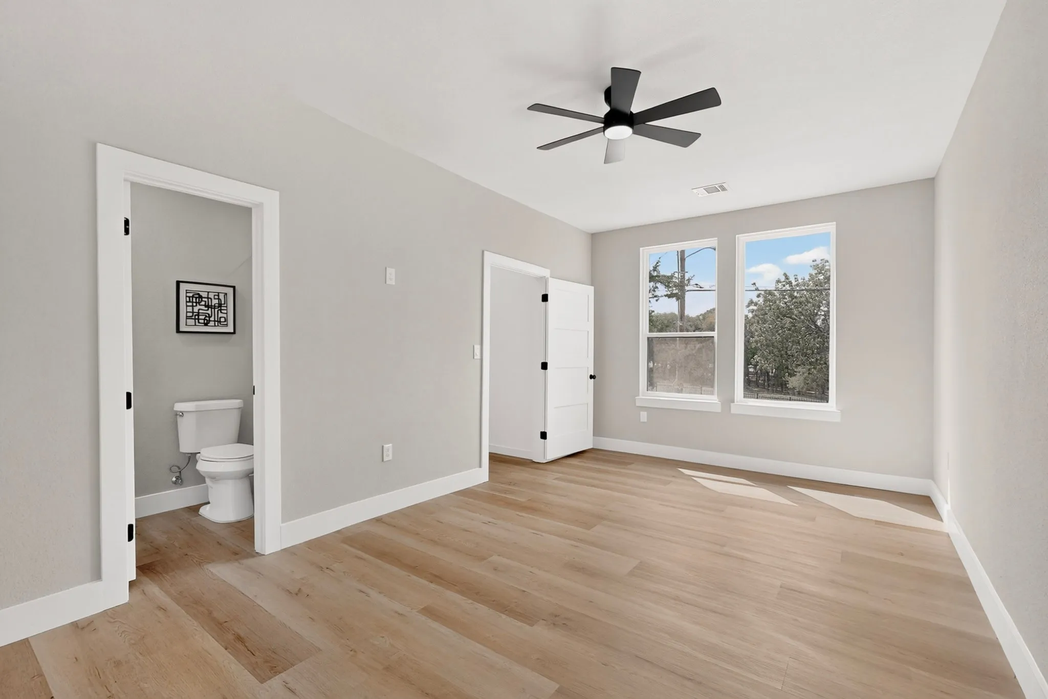 Light-toned wood-finish flooring, white trim, and a black ceiling fan with integrated lighting