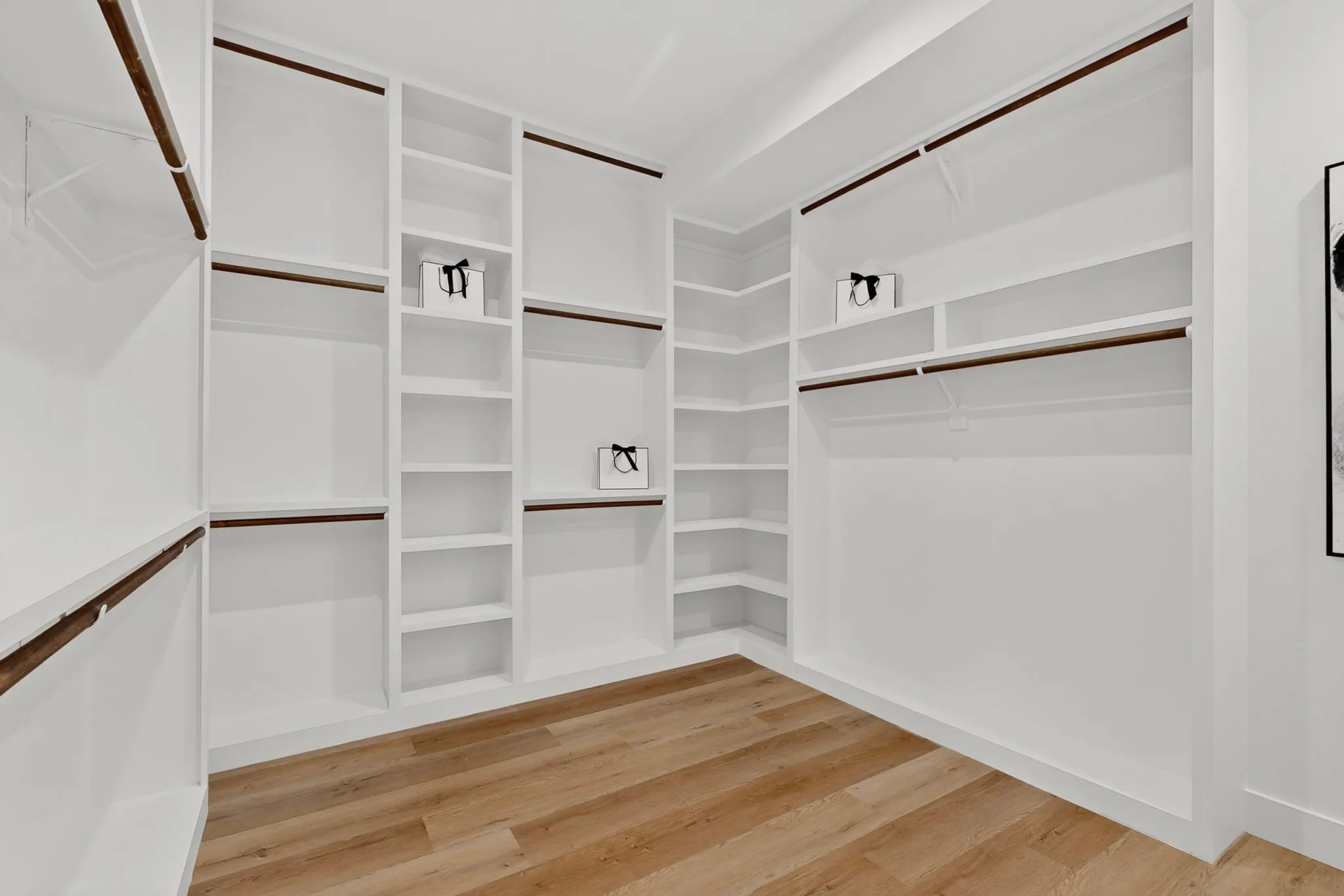 Custom built-in white shelving, integrated hanging rods, corner shelving unit, full-height storage, and wood-finish flooring