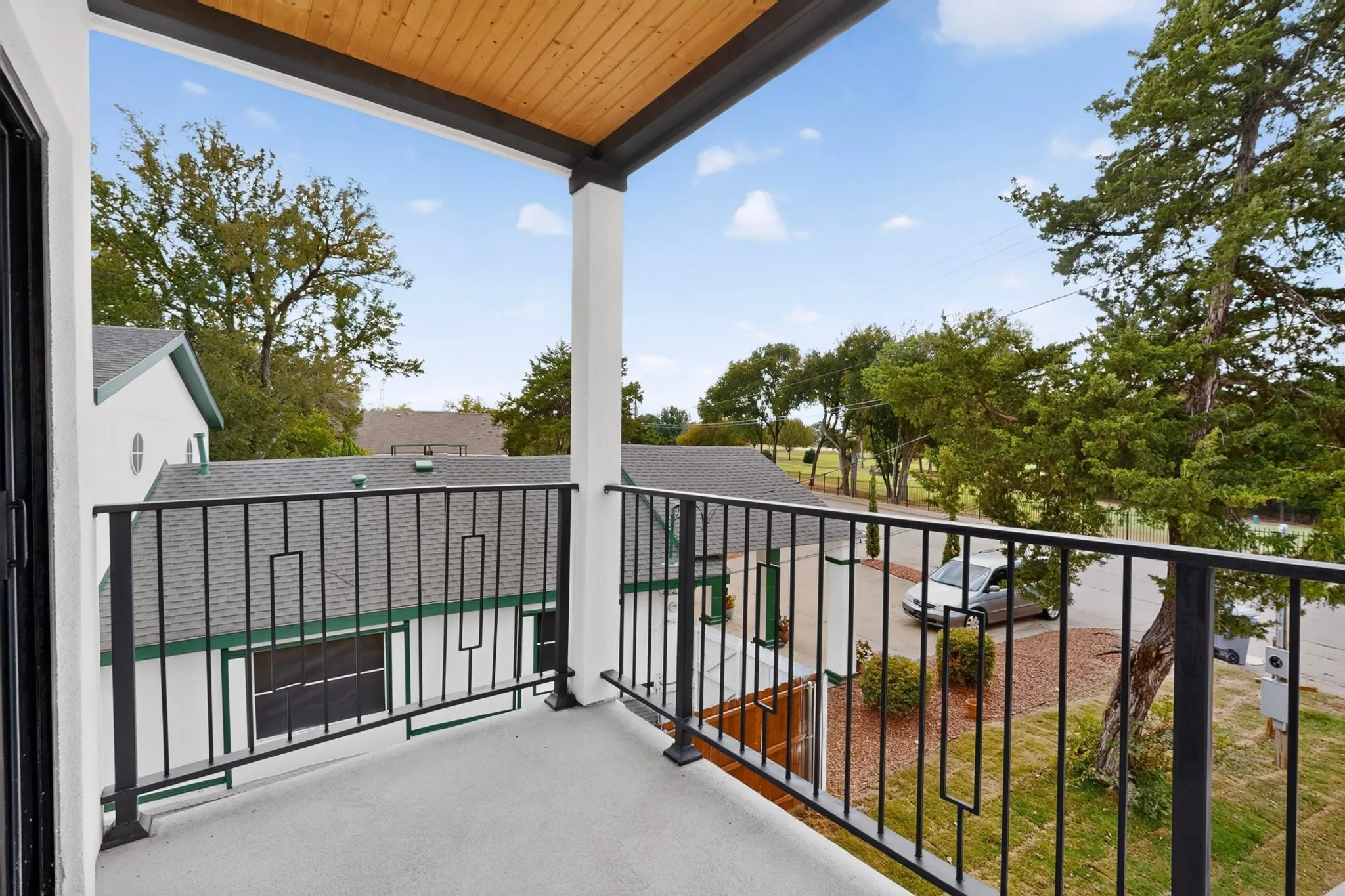 Balcony with black metal railing, wood-paneled ceiling, and concrete flooring