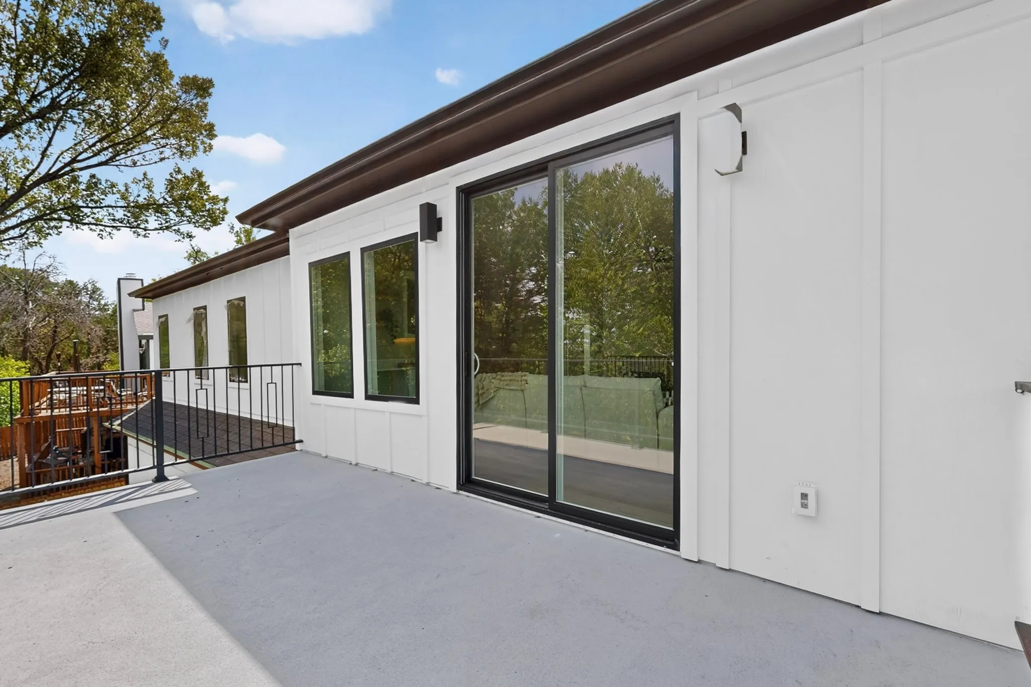 Exterior deck with a black metal railing, adjacent to a white facade with multiple windows and a sliding glass door