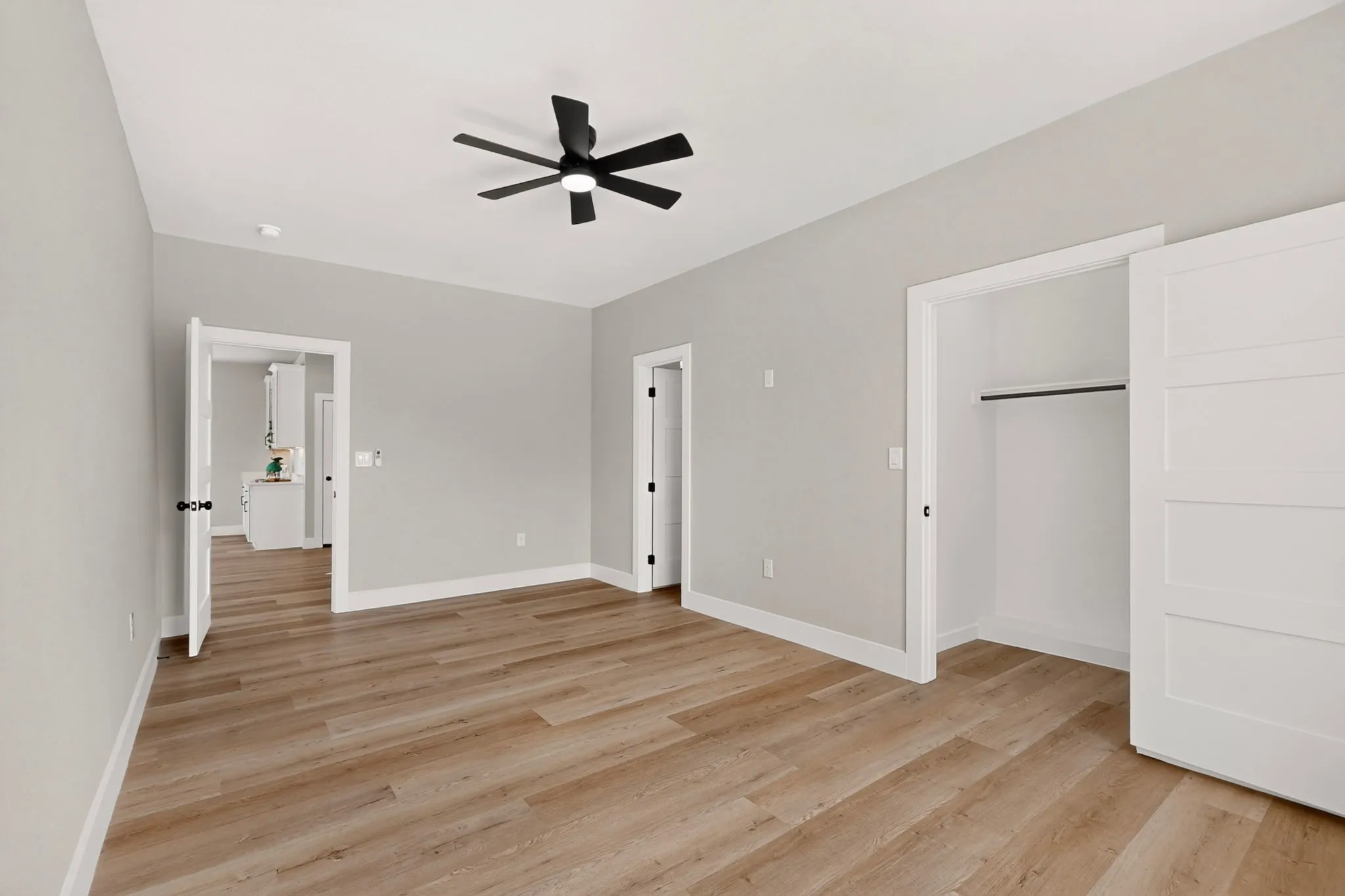 Wood-finish flooring with white trim, a ceiling fan, and a built-in closet with sliding panel doors