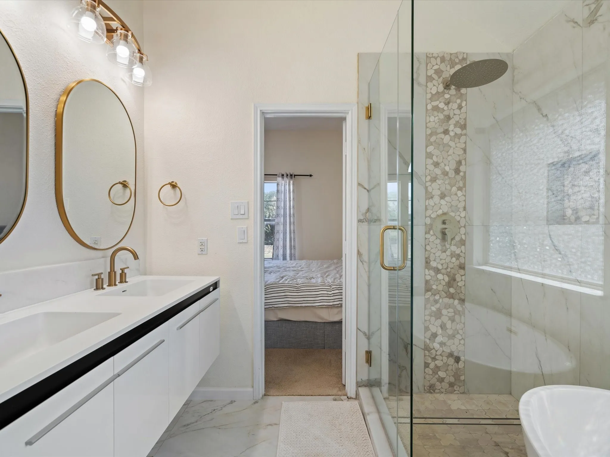 Ensuite bathroom featuring double vanity, a marble finish shower, and light marble finish flooring