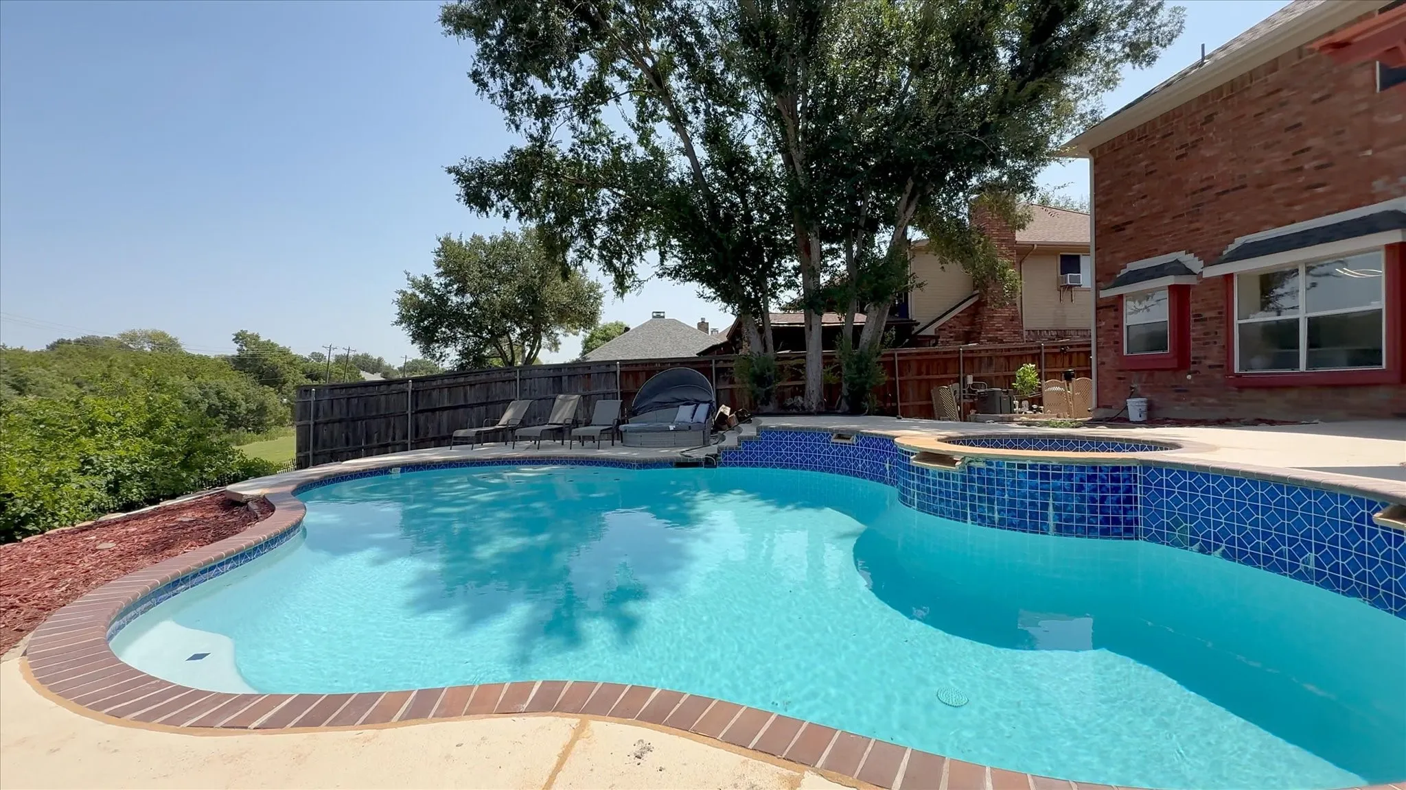 Backyard oasis featuring a curvilinear swimming pool with blue mosaic tile accents, integrated spa, and concrete decking
