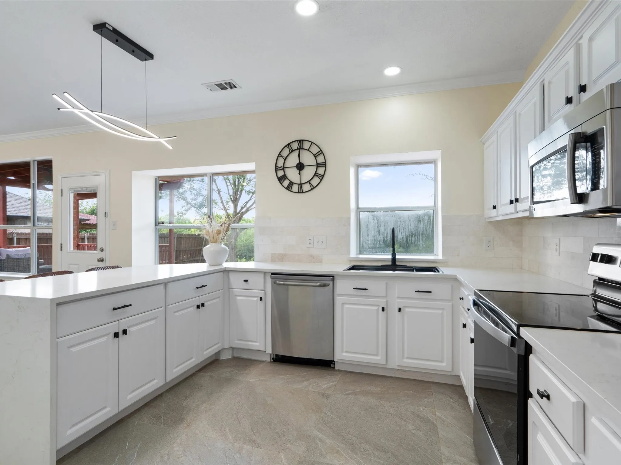 Kitchen with appliances with stainless steel finishes, crown molding, white cabinetry, decorative light fixtures, and tasteful backsplash