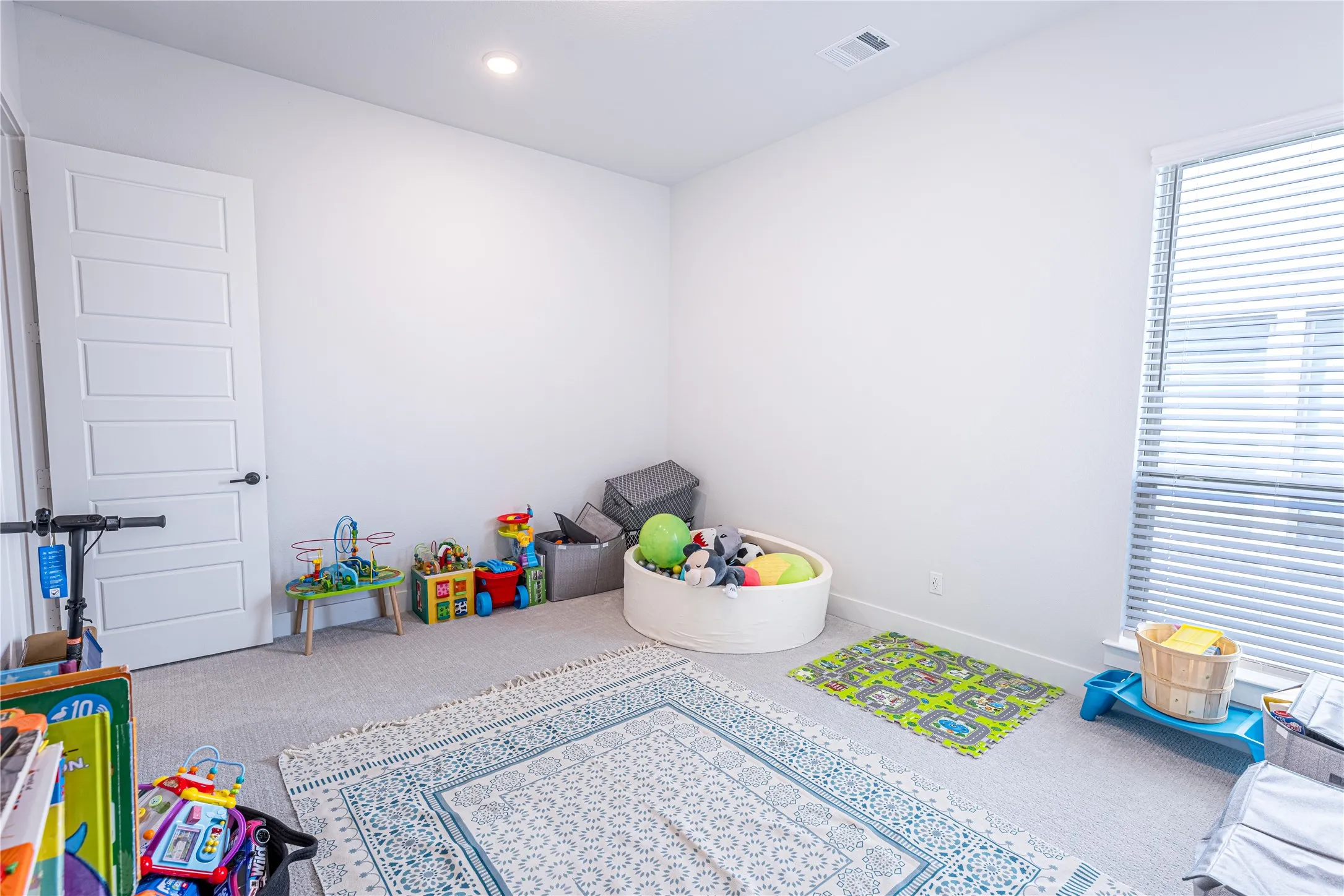 Light-filled room featuring a single window with horizontal blinds, neutral wall paint, and a white paneled door with matte black hardware