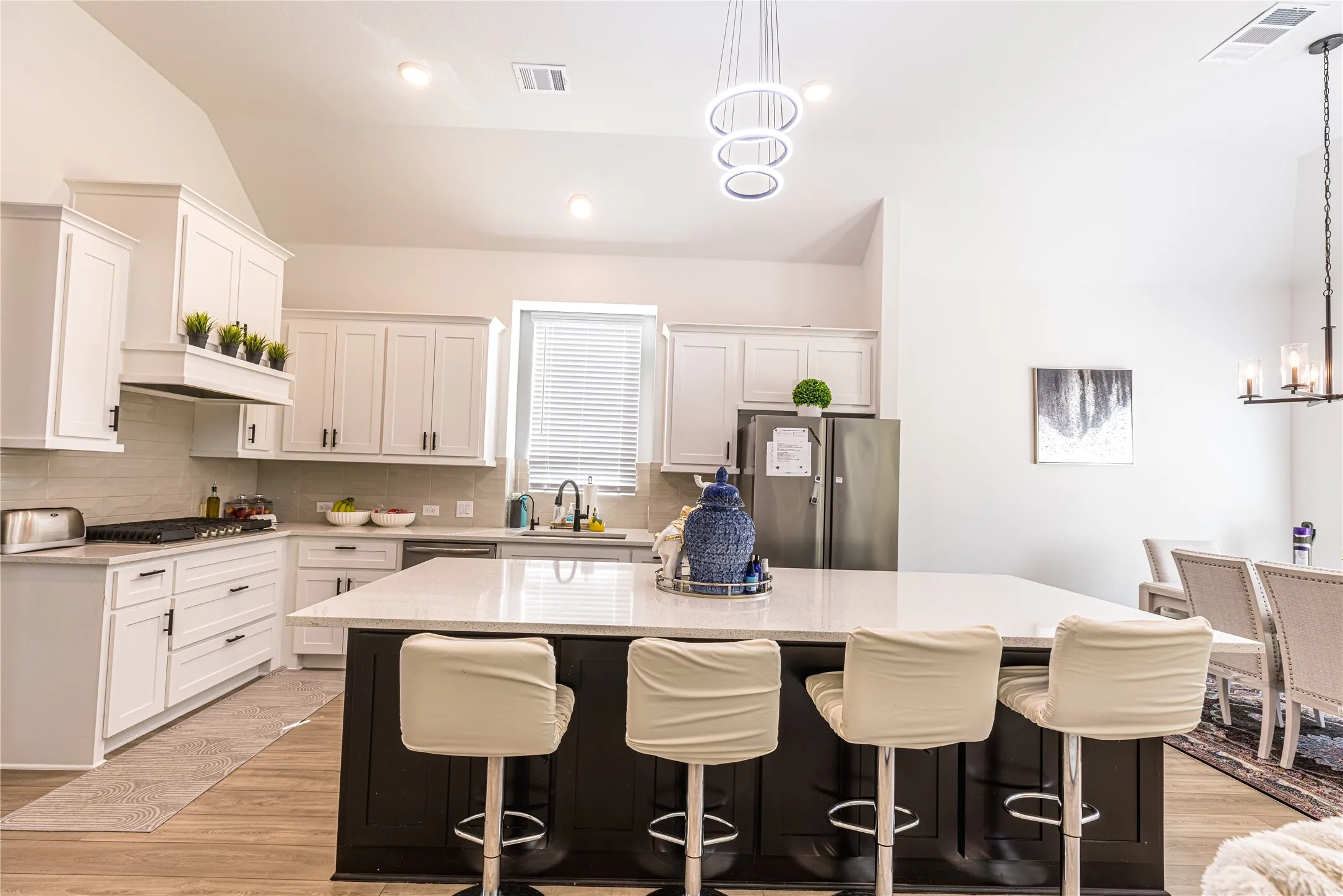 Kitchen featuring a large island with a light-toned countertop, white cabinetry with dark hardware, stainless steel appliances, and wood-finish flooring