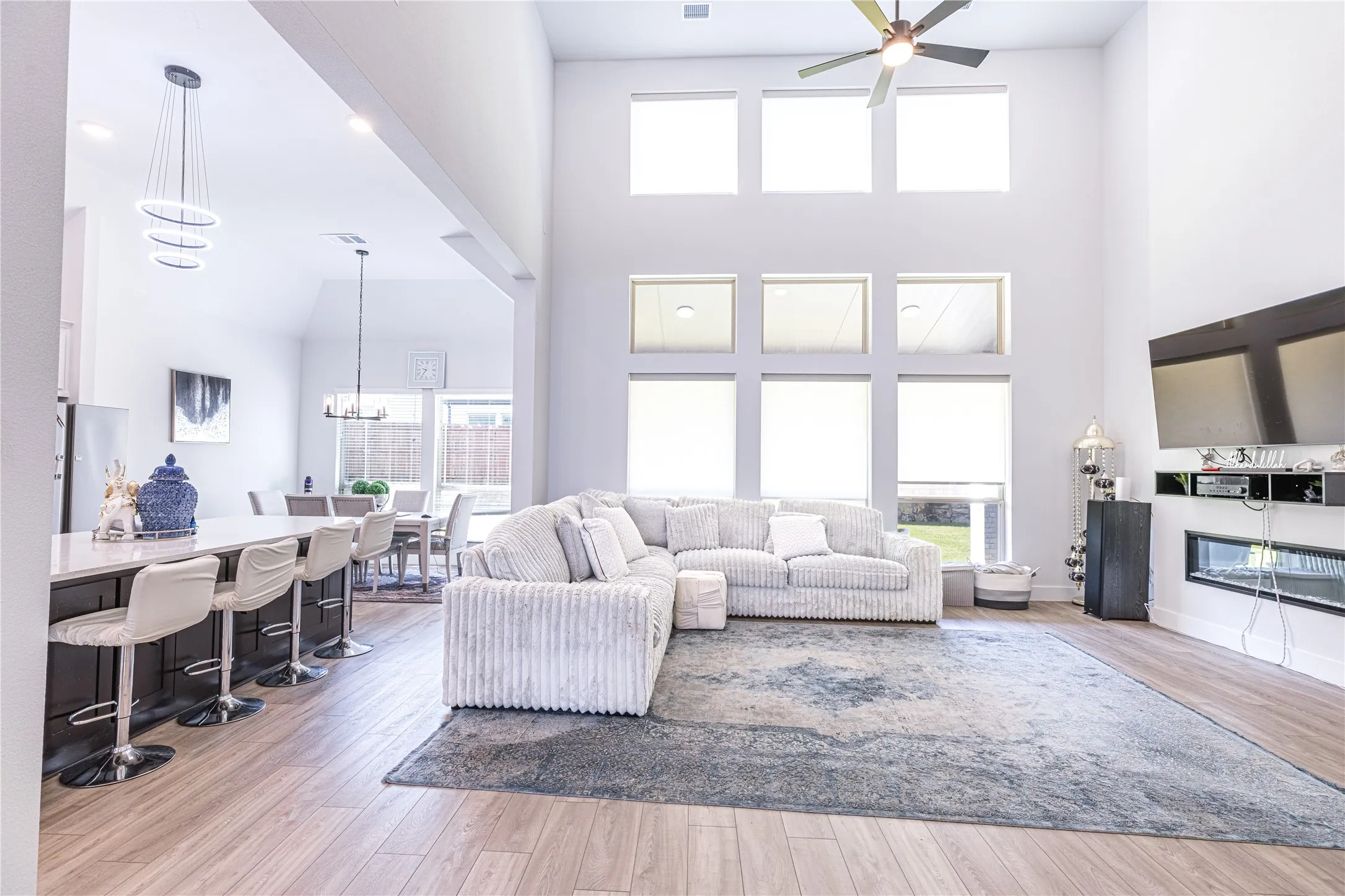 Double-height living space featuring wood-finish flooring, a contemporary ceiling fan, and a built-in linear electric fireplace