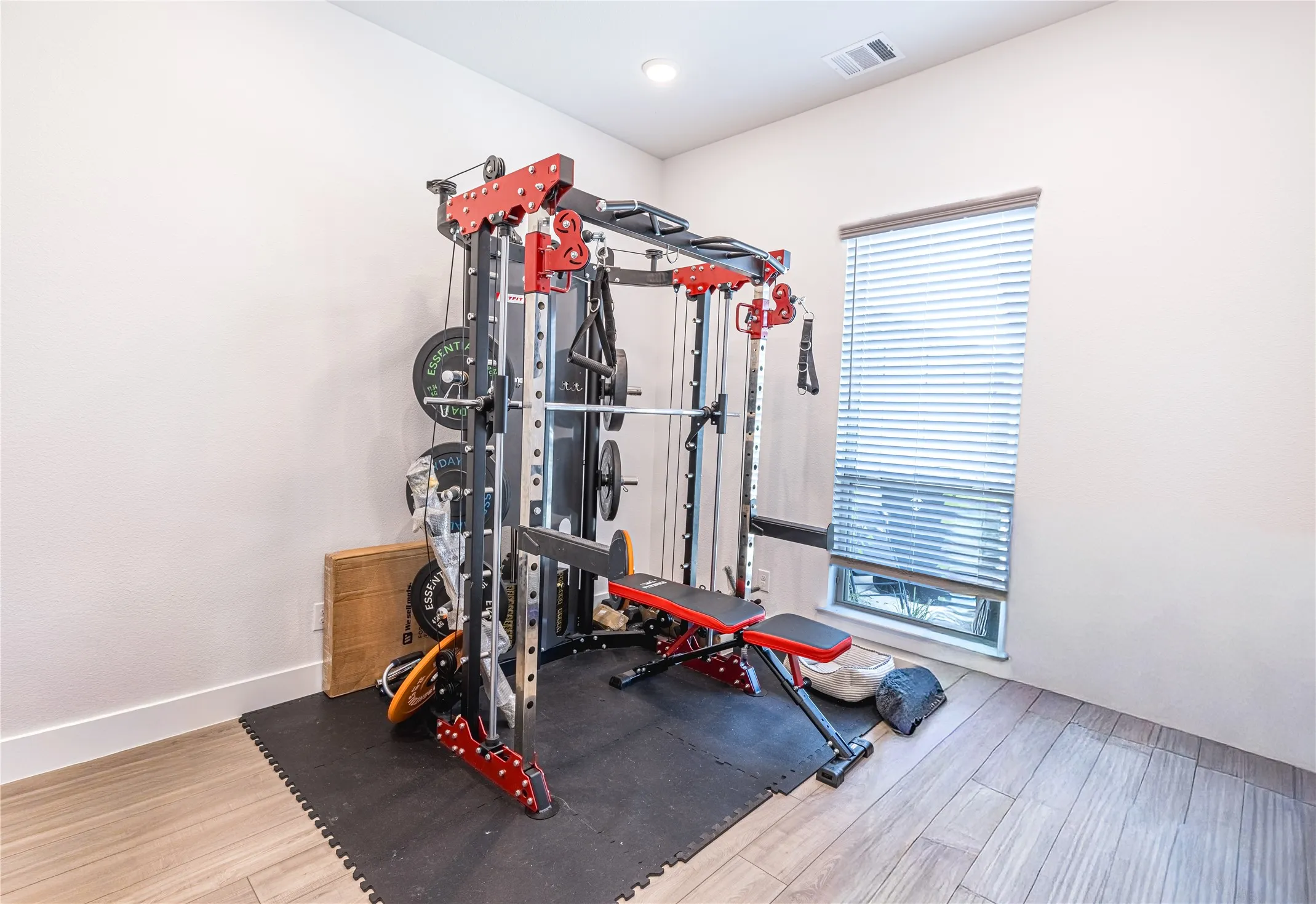 Room featuring light neutral walls, recessed lighting, wood-finish flooring, a single window with blinds, and a dedicated area with interlocking rubber mat flooring