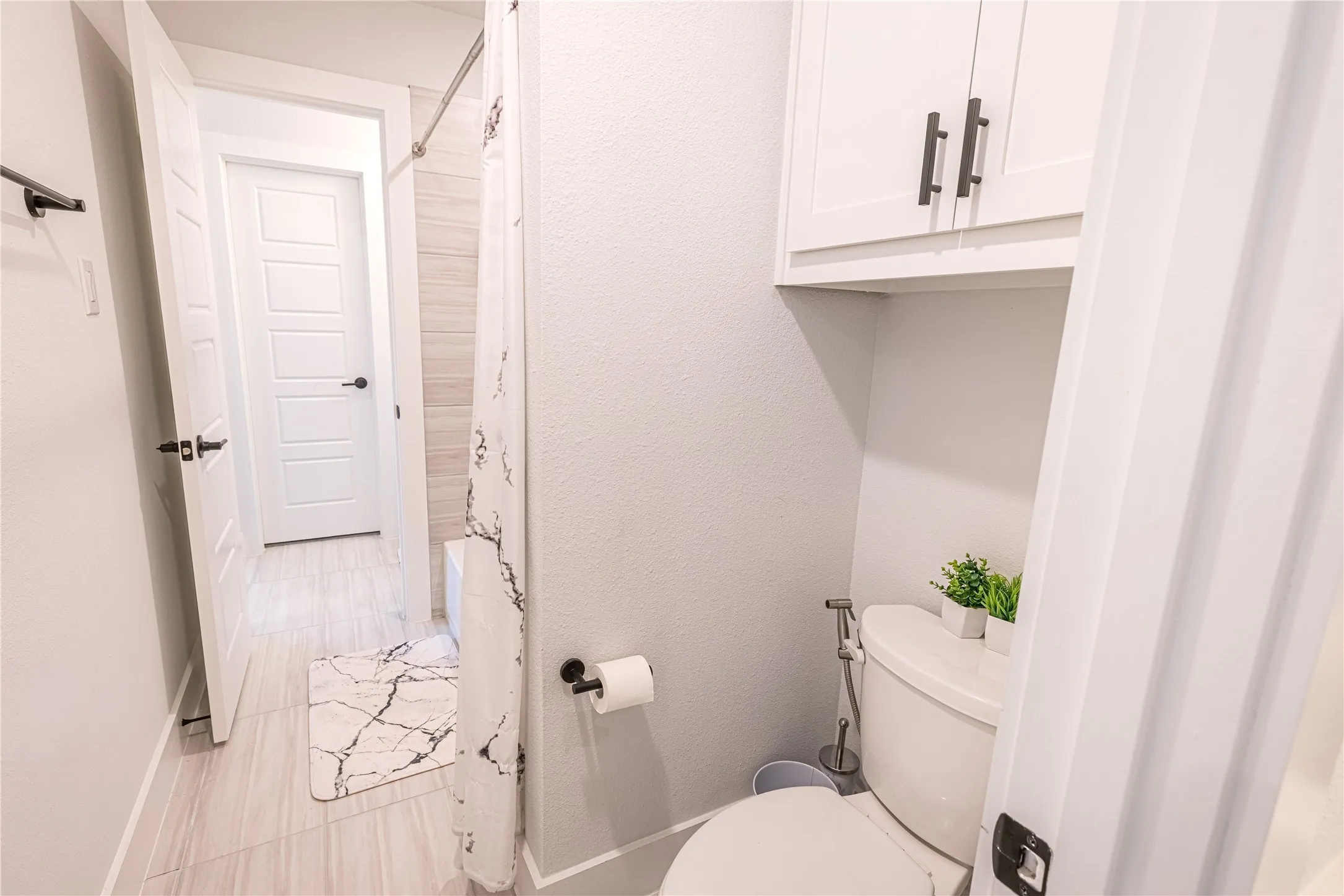 Full bathroom featuring a white toilet with an overhead storage cabinet, a shower with a tiled surround, and light-toned tile flooring