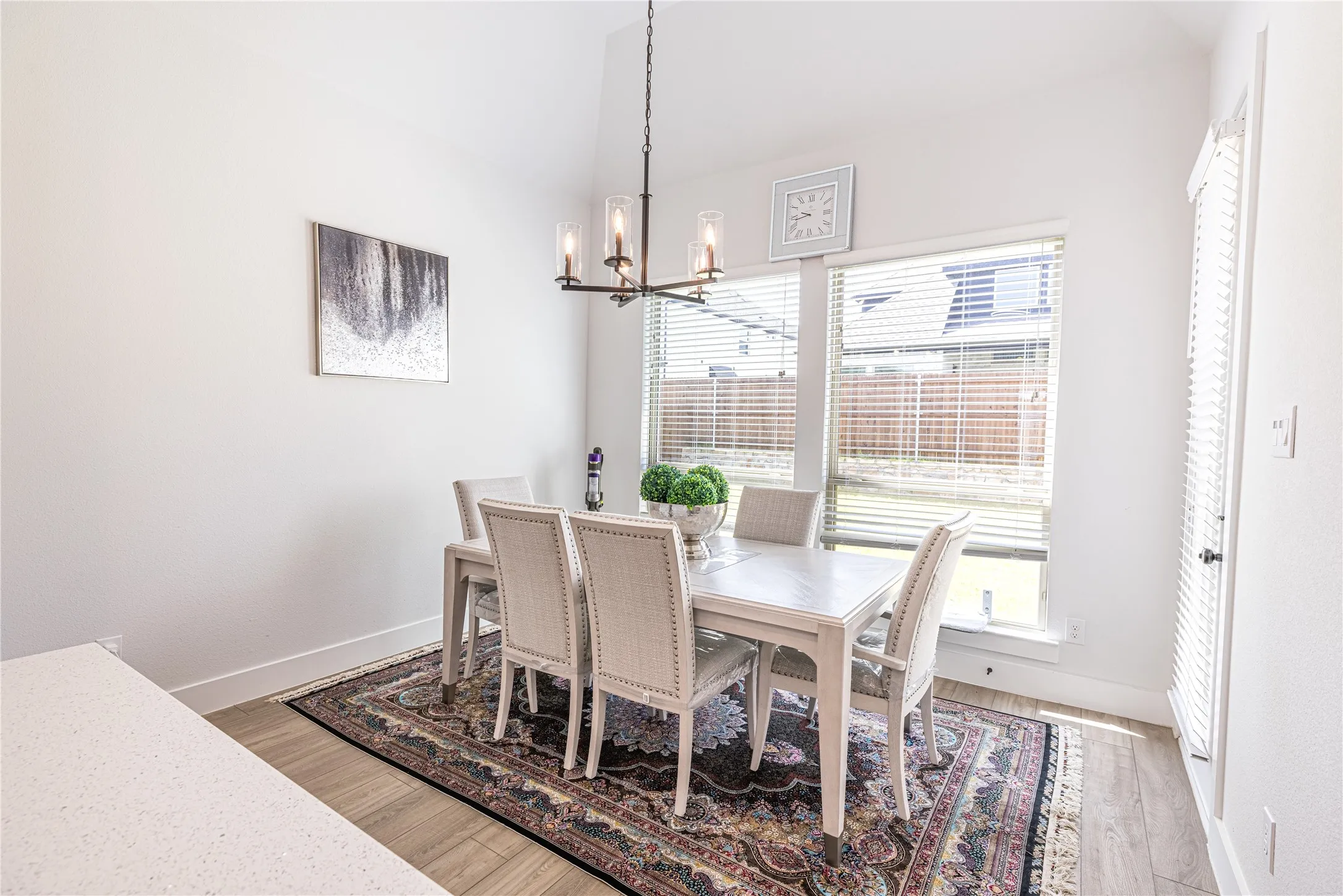 Dining area featuring vaulted ceilings, wood-finish flooring, a contemporary chandelier, and a large window with horizontal blinds