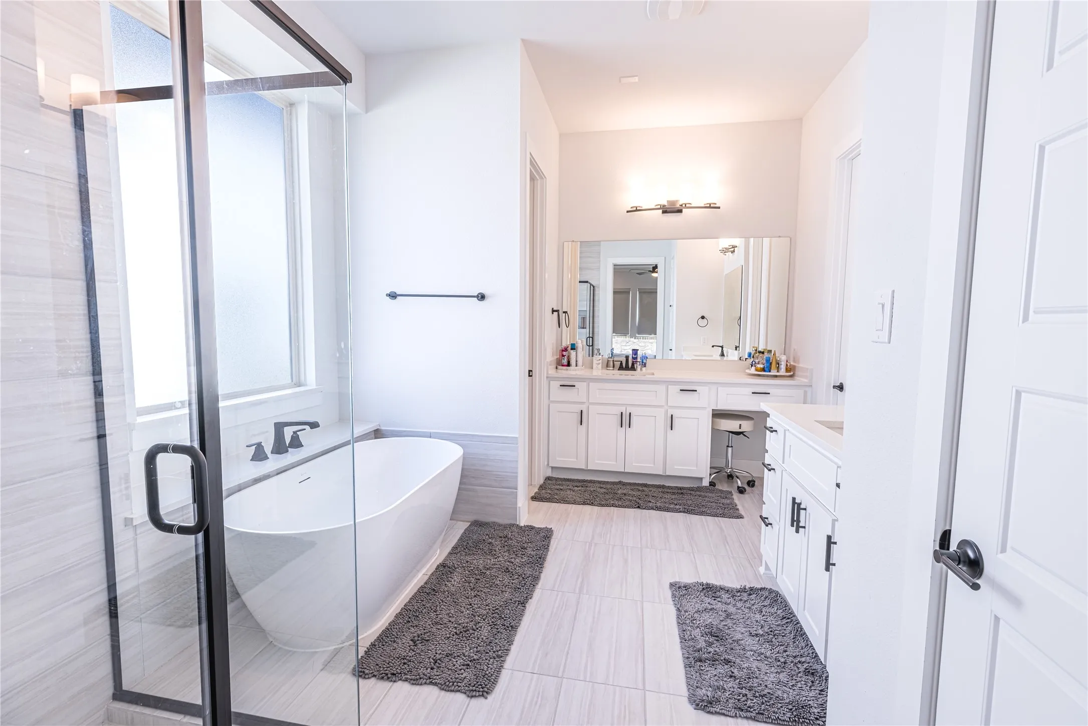Modern bathroom featuring a freestanding tub, glass-enclosed shower with tile surround, dual vanities with white cabinetry, and large mirrors