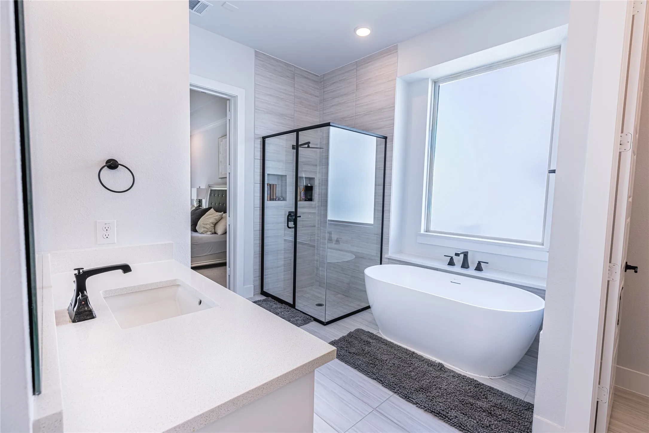 Bathroom featuring a freestanding soaking tub, a frameless glass shower enclosure with built-in niches, a vanity with a white countertop and integrated sink, and matte black plumbing fixtures