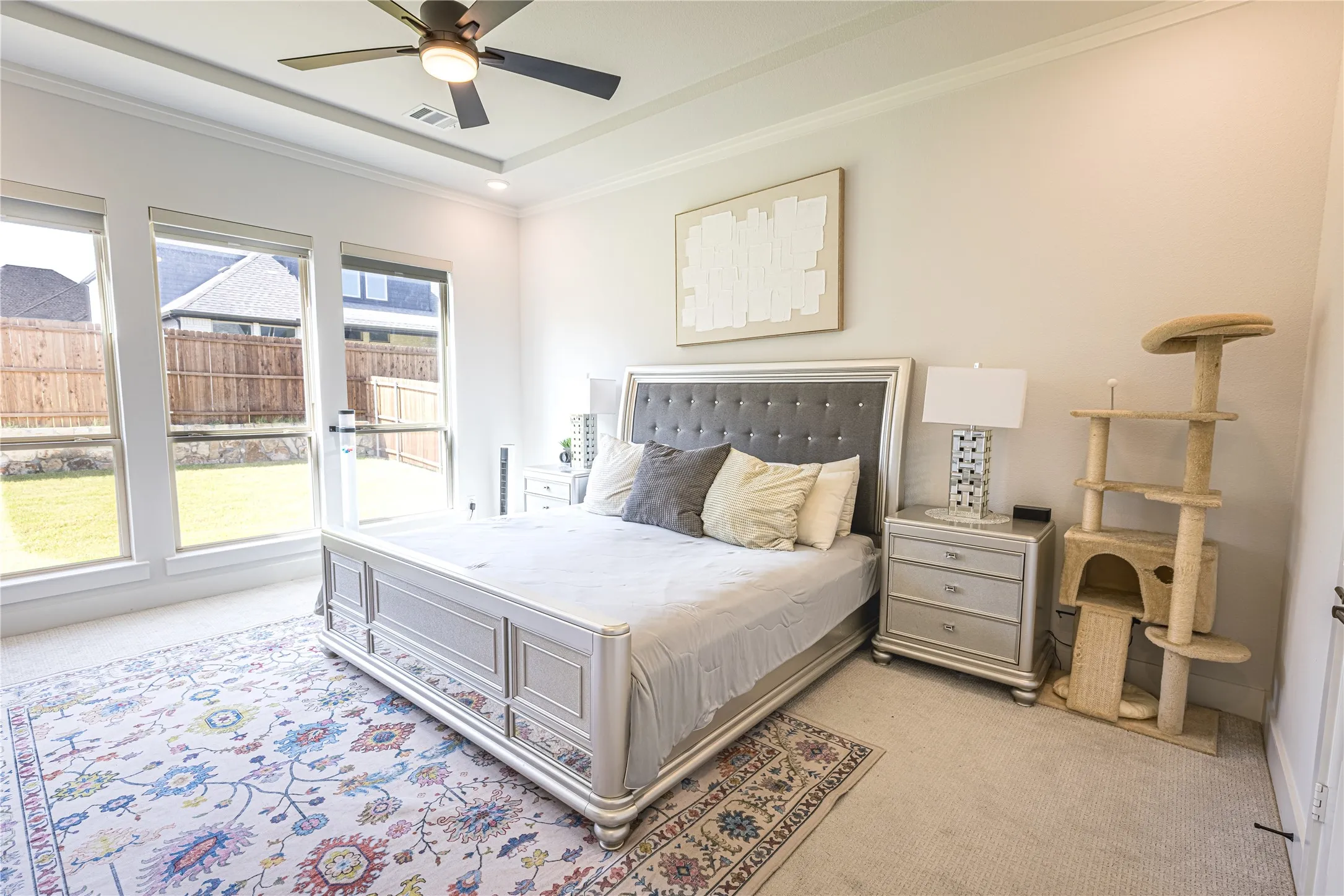 Spacious room featuring multiple large windows providing abundant natural light, tray ceiling with a ceiling fan, and light-toned carpet flooring