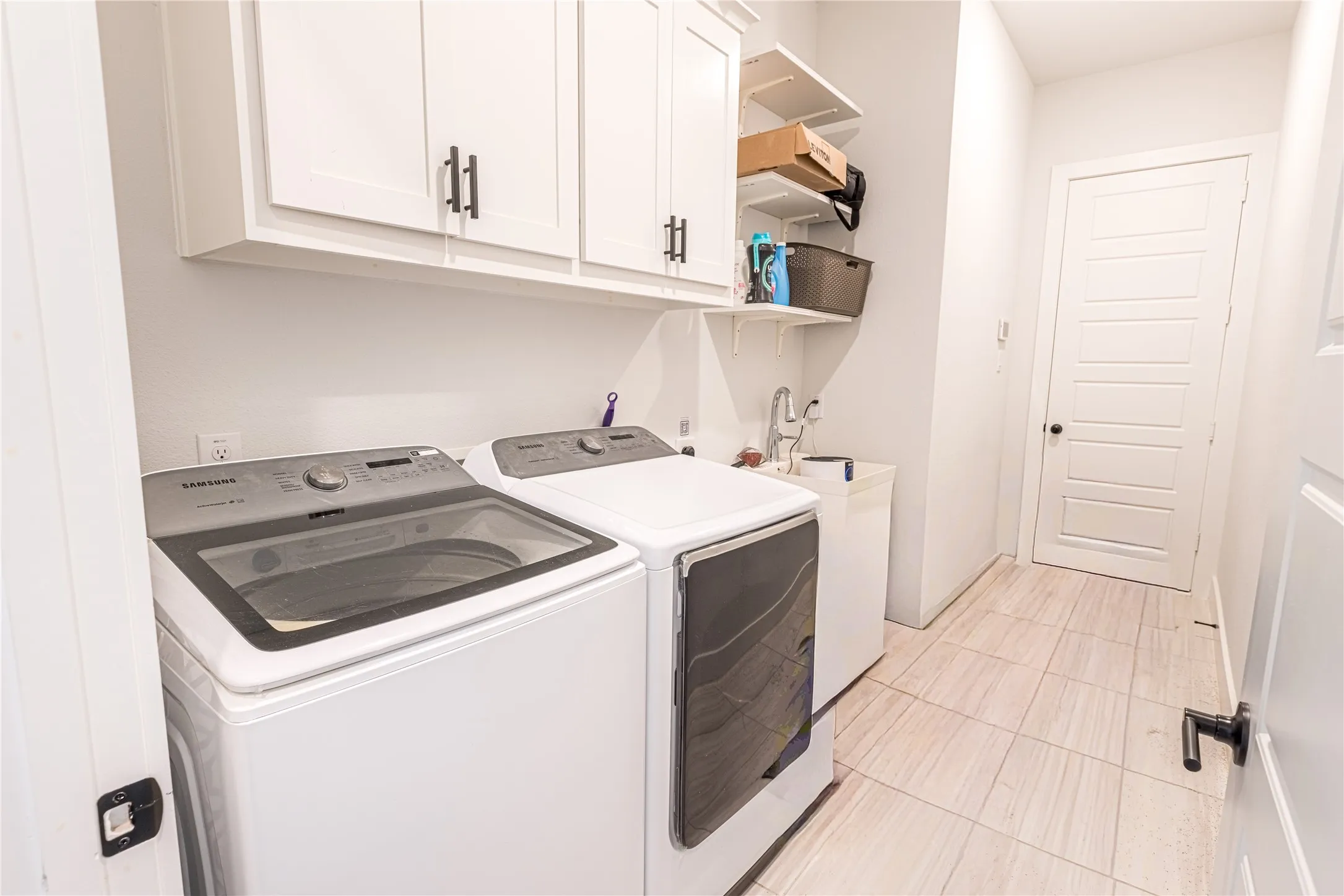 Laundry area featuring white cabinetry, open shelving, a utility sink, and light-toned tile flooring