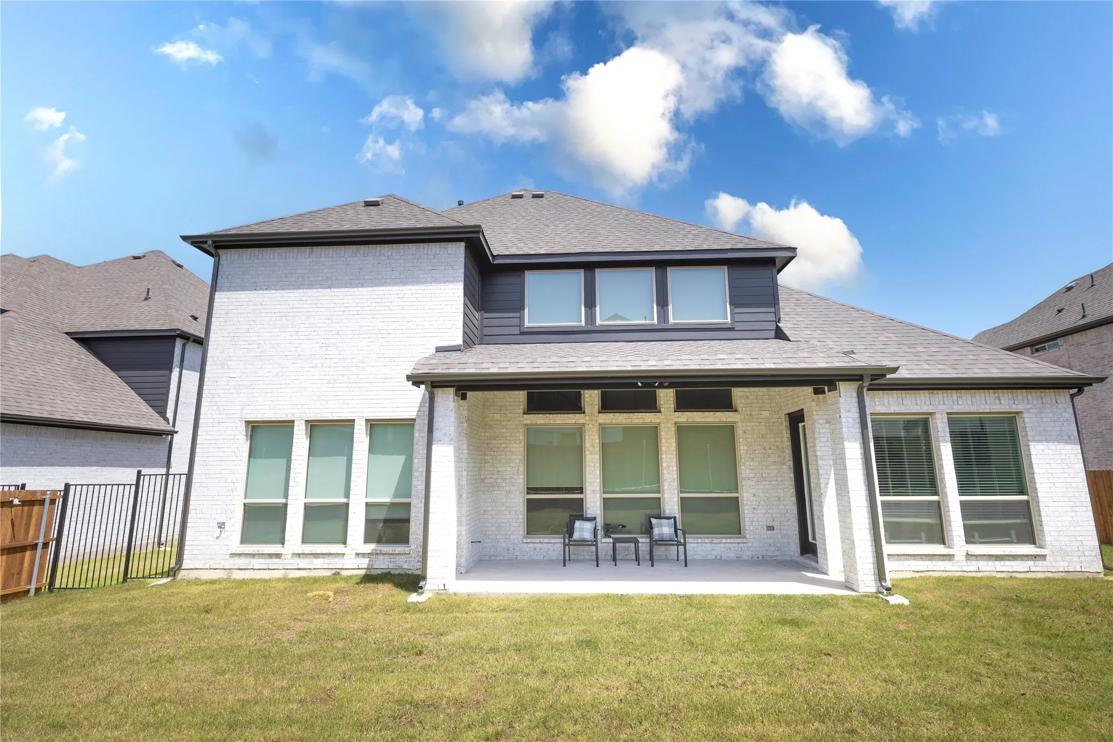 Rear exterior featuring a covered patio, extensive windows, and a manicured lawn
