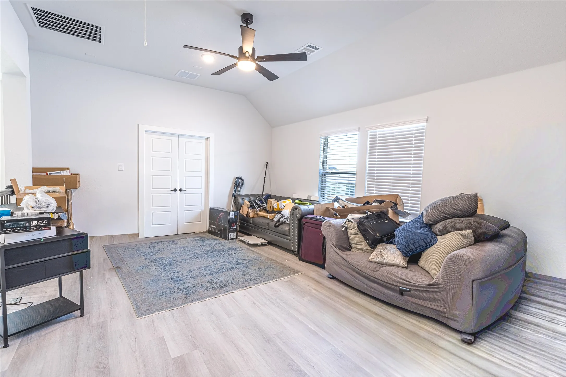 Spacious room featuring light wood-finish flooring, a vaulted ceiling, and a contemporary ceiling fan