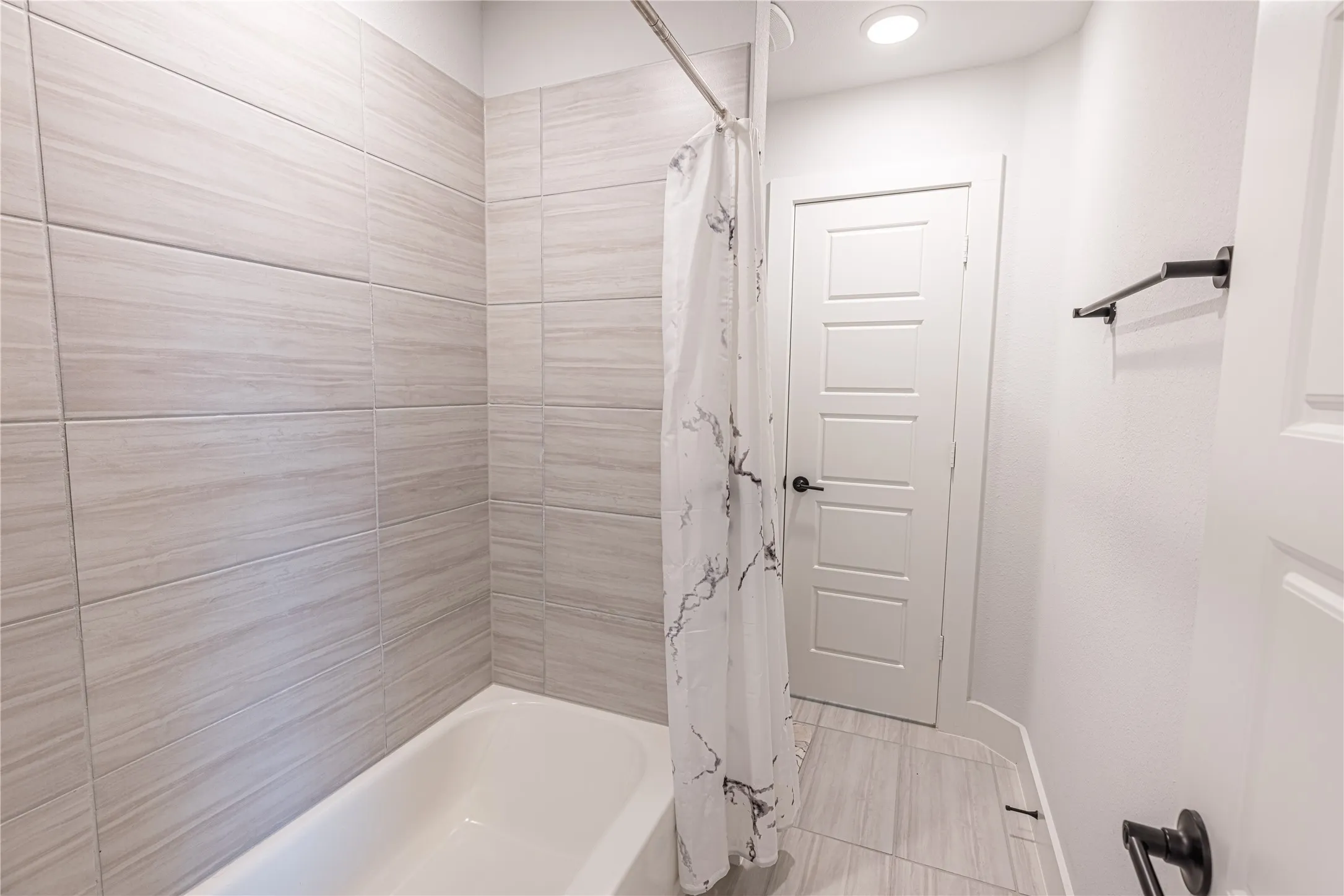 Bathtub with light-toned horizontal wall tiles, complemented by coordinating floor tiles