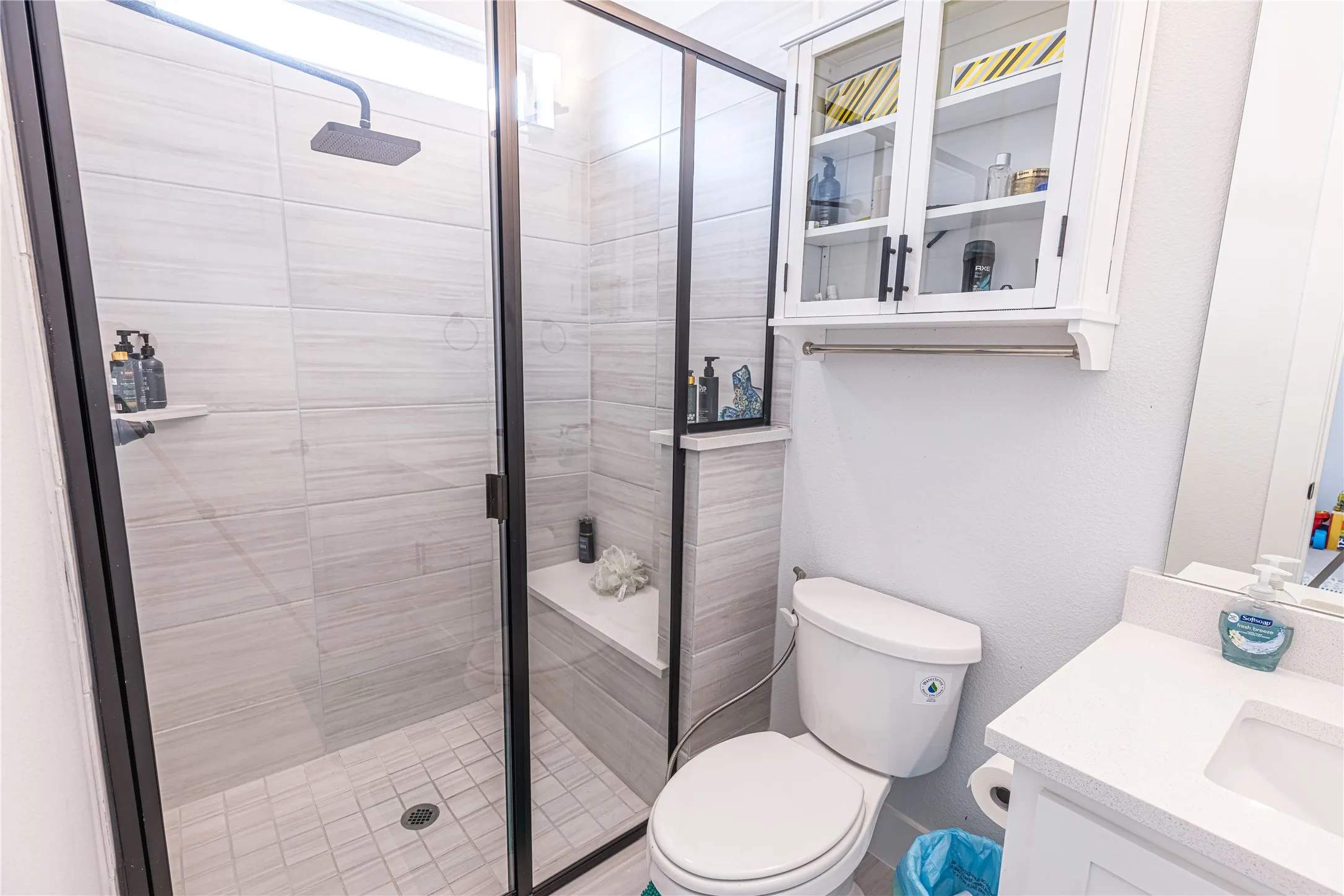 Modern bathroom featuring a glass-enclosed shower with light-toned tile, a built-in shower bench, and a rain shower head