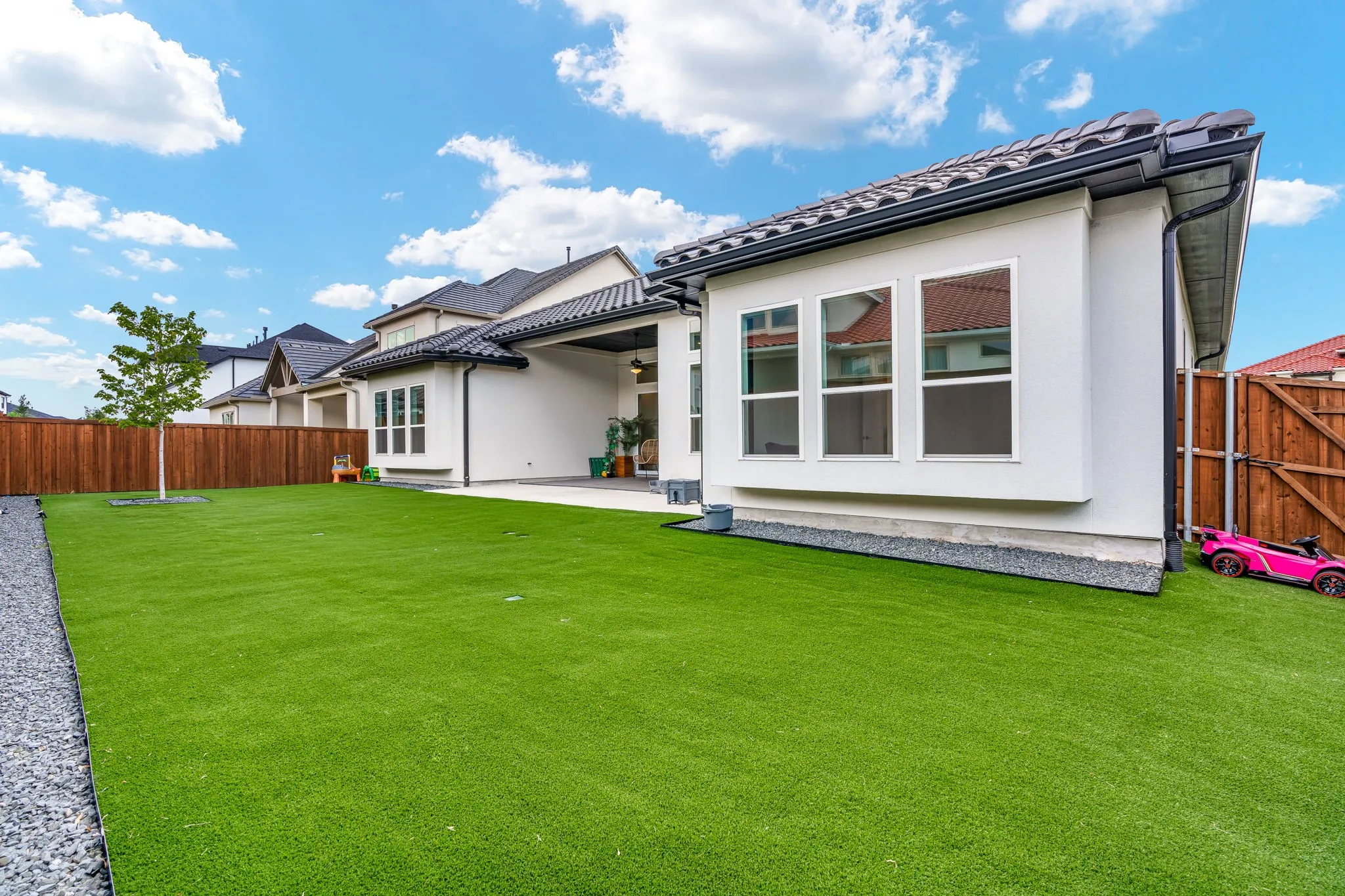 Expansive backyard featuring artificial turf, a gravel border, and a wood privacy fence