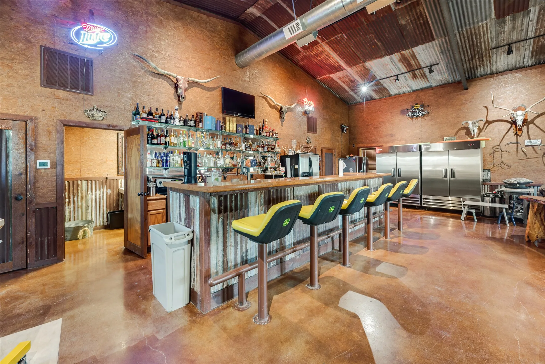 Custom bar area featuring a wood-finish countertop, corrugated metal paneling, and a full-size back bar with glass shelving