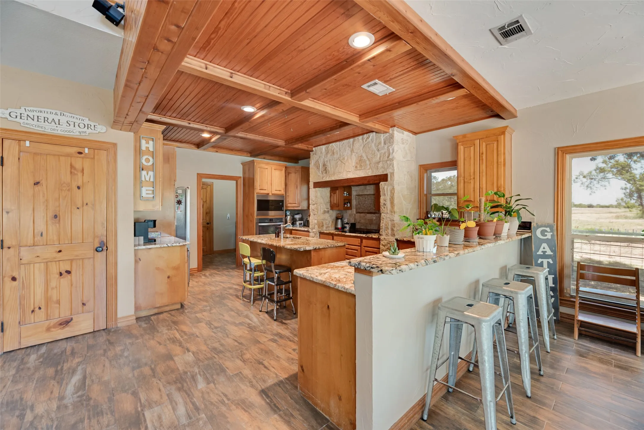 Kitchen featuring a plank wood-finish ceiling with exposed beams, stone accent walls, wood-finish cabinetry, and granite countertops