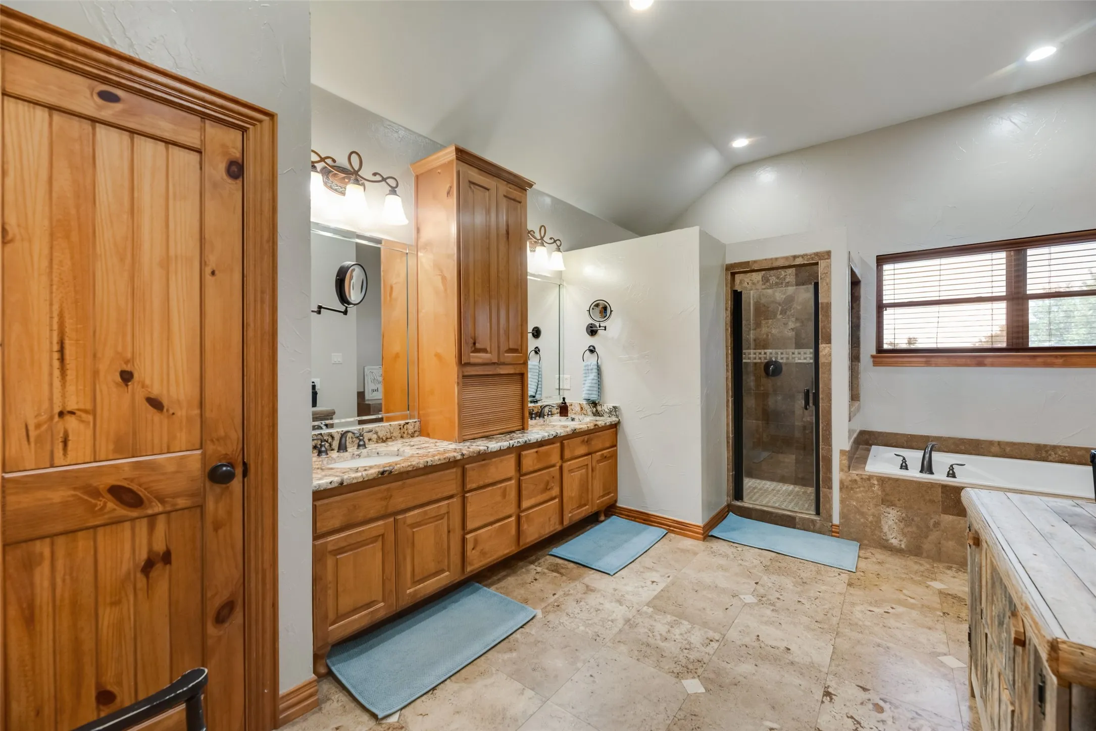Primary bathroom featuring a dual vanity with light-toned countertops, a glass-enclosed shower, a built-in soaking tub, and natural wood cabinetry
