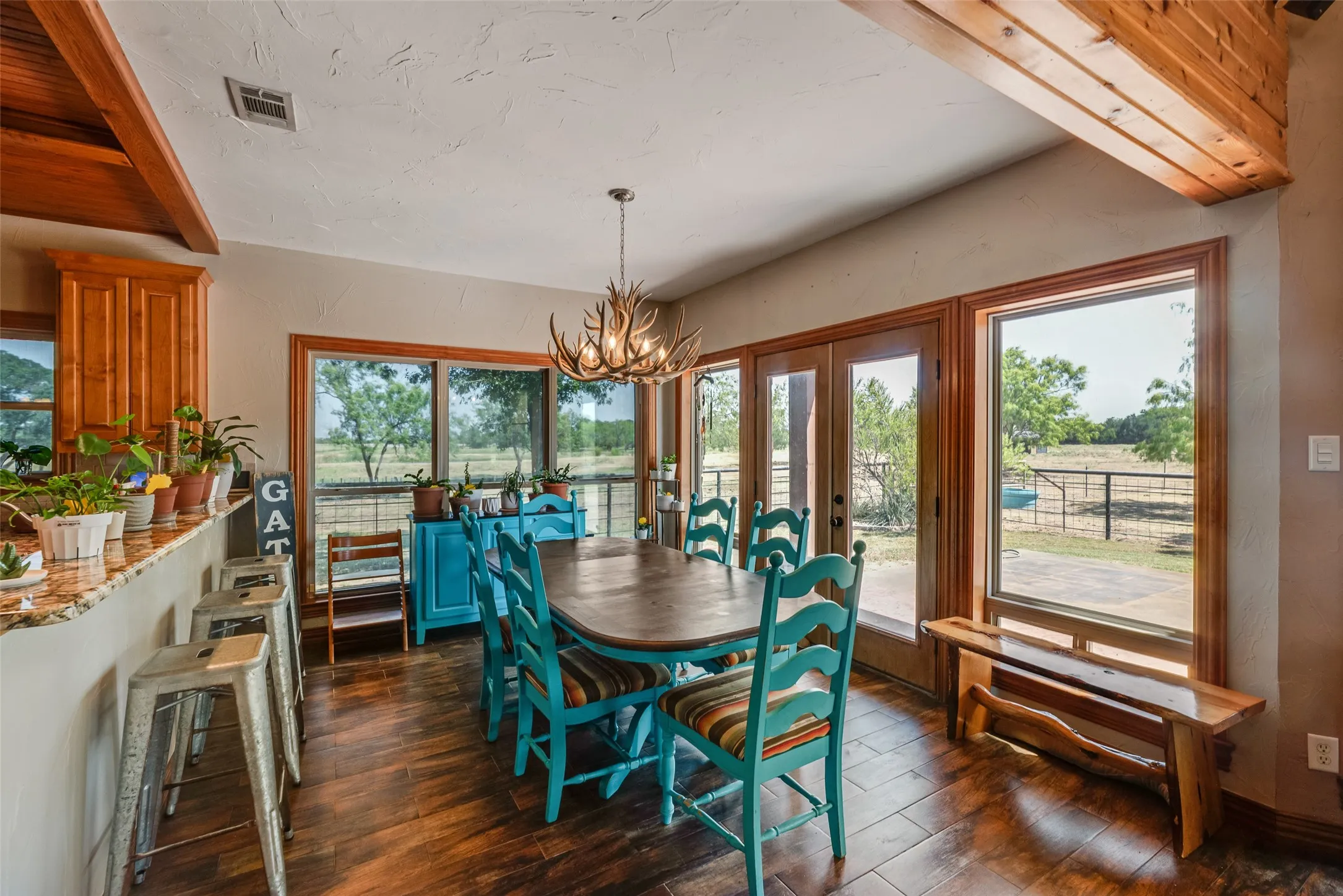 Dining area featuring wood-finish flooring, wood-framed windows, double glass doors, a decorative chandelier, and exposed wood beams