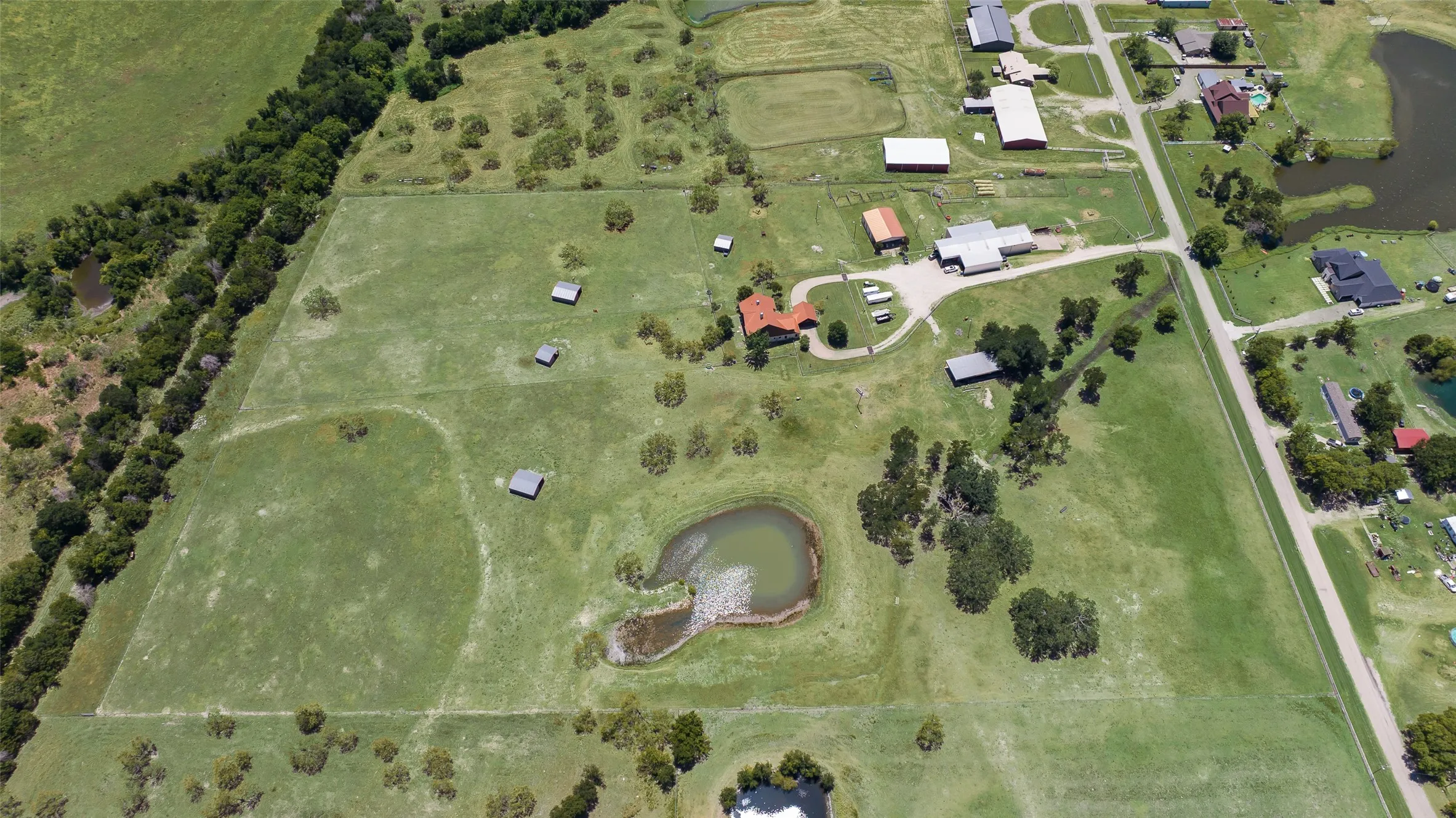 Expansive aerial view showcasing a large land parcel with multiple structures and a pond