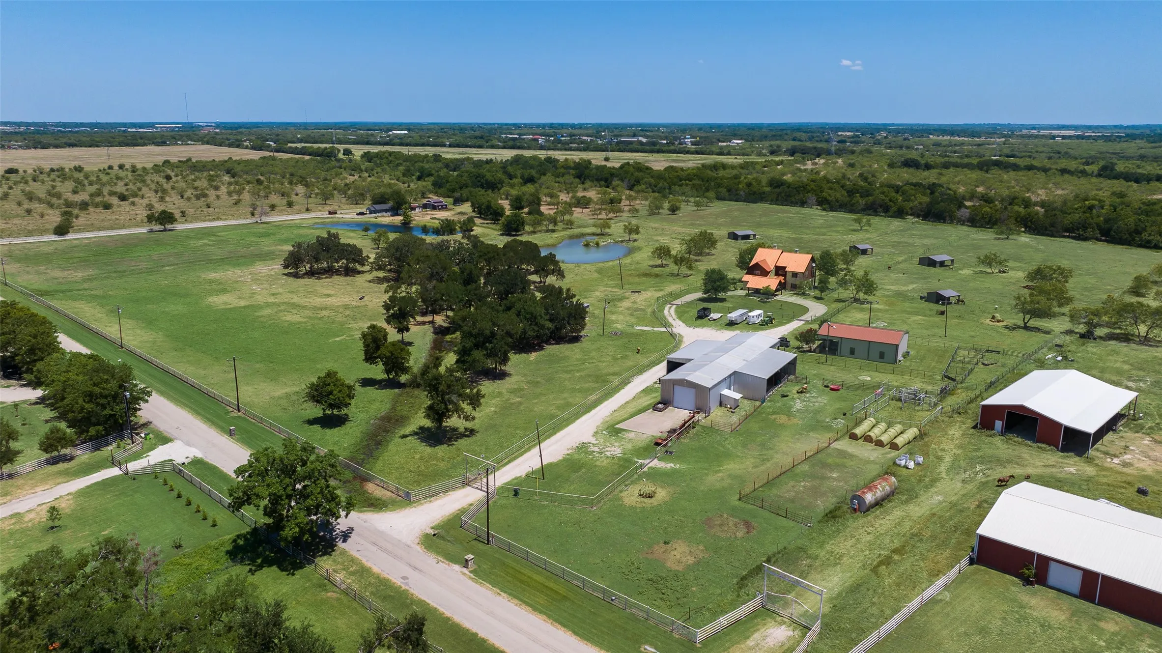 Expansive property featuring multiple structures, including a prominent orange-roofed residence, a large silver-roofed outbuilding, and a red barn