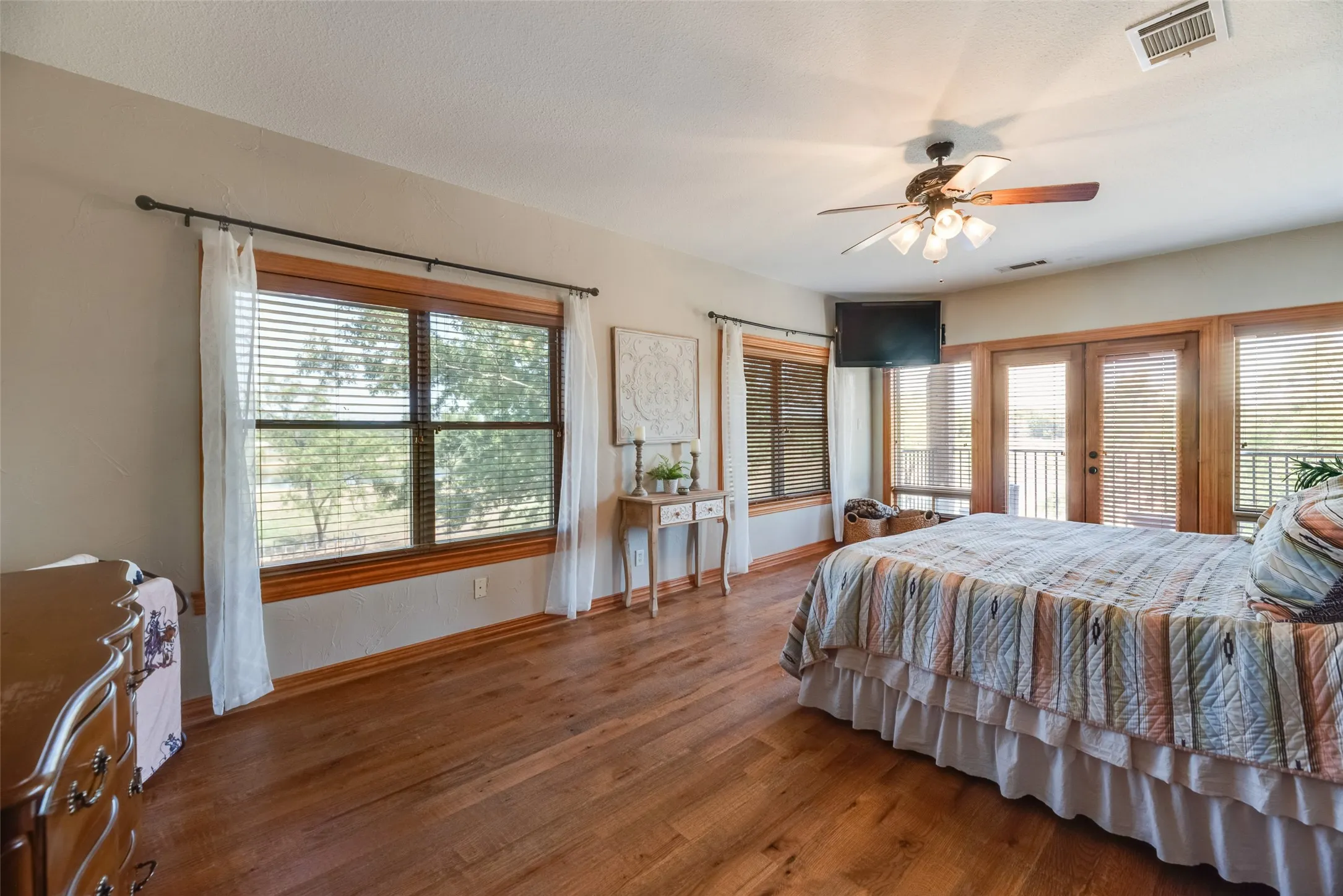 Hardwood-finish flooring throughout, featuring multiple windows with wood trim, and direct access to an exterior balcony via double French doors