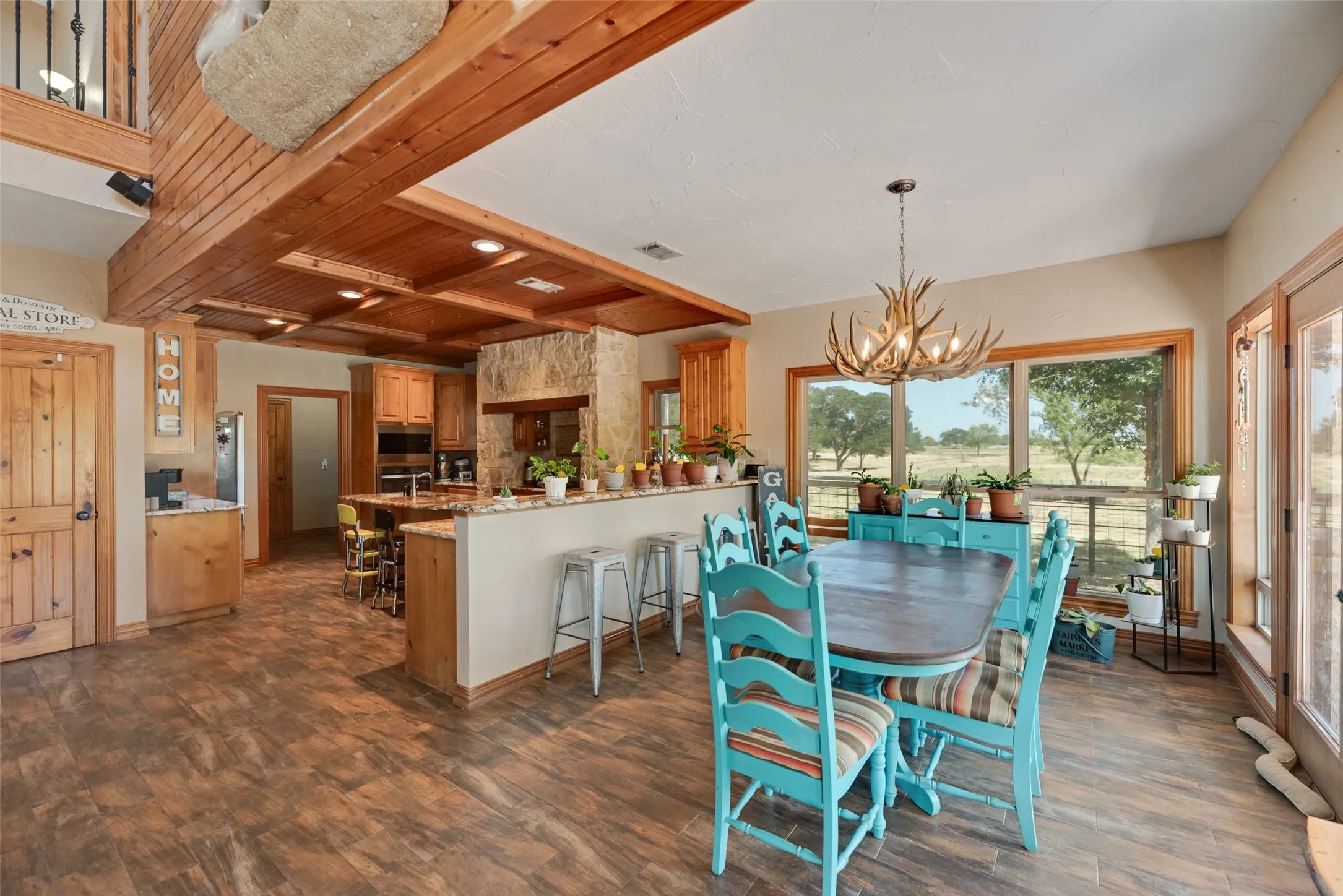 Open-concept interior featuring wood-finish flooring, a kitchen island with stone countertops, natural wood cabinetry, and a stone-clad kitchen wall