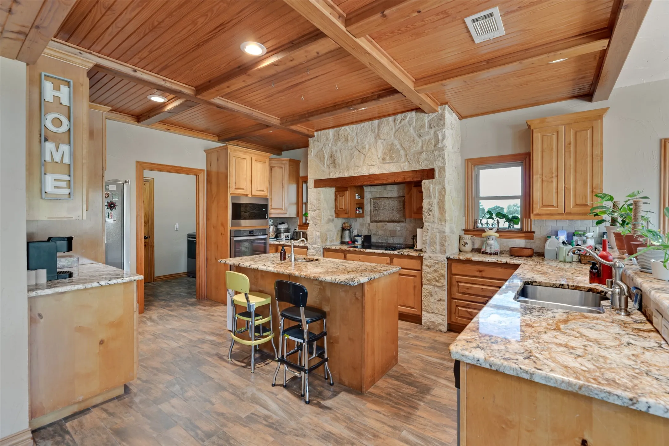 Kitchen featuring a wood-panel ceiling with exposed beams, wood-finish flooring, and a stone-clad accent wall