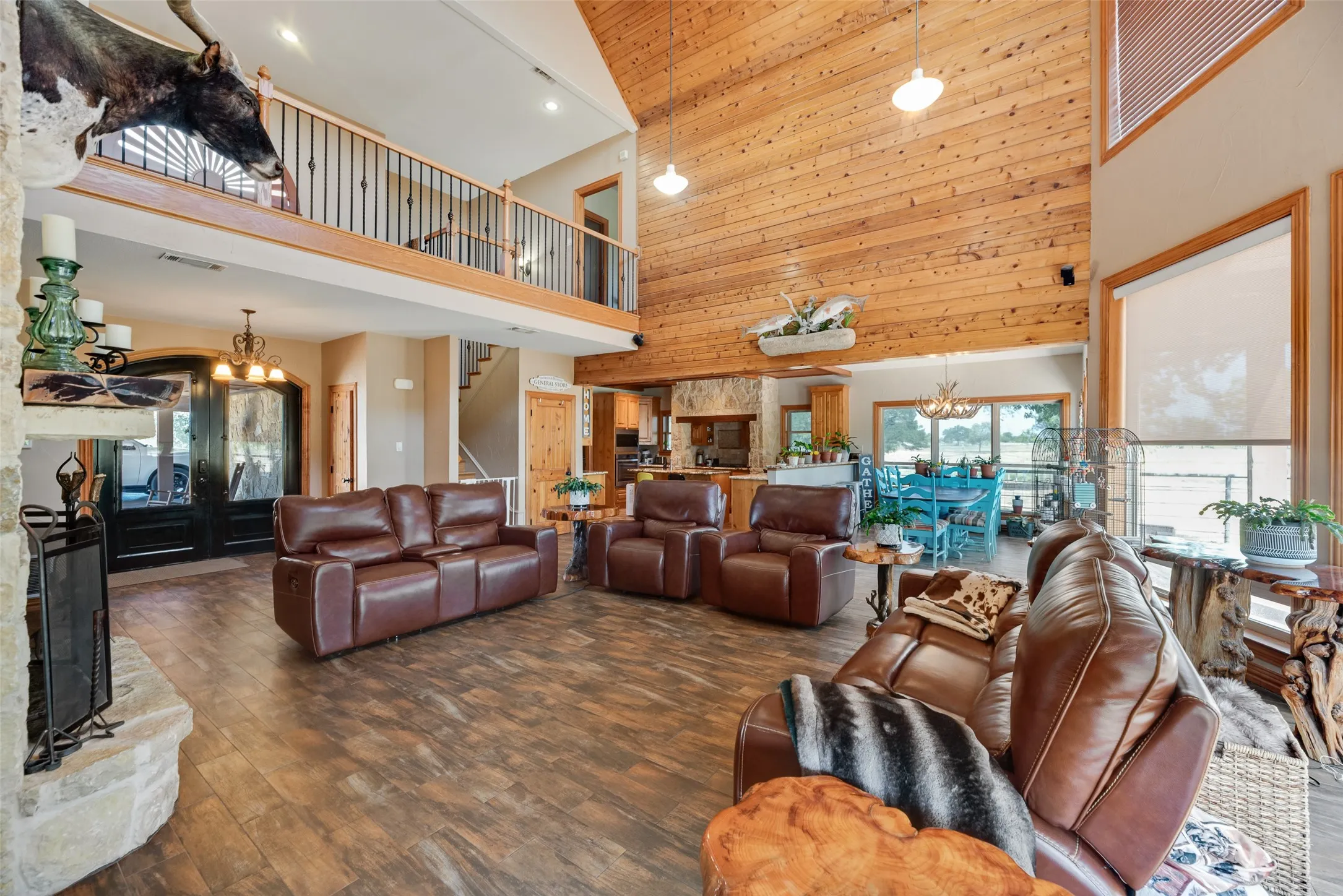 Spacious living area featuring wood-finish flooring, a stone-clad fireplace, and a vaulted wood-paneled ceiling