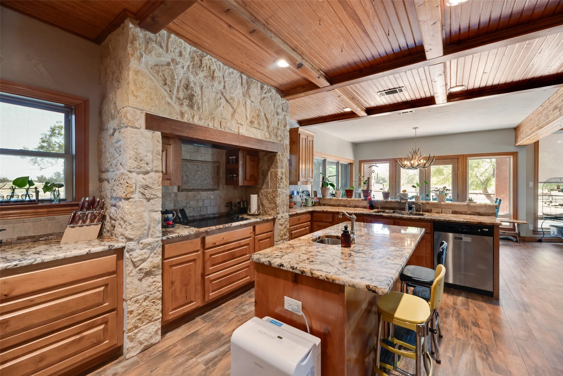 Expansive kitchen with a stone-clad range hood, wood-finish flooring, and a beamed wood ceiling