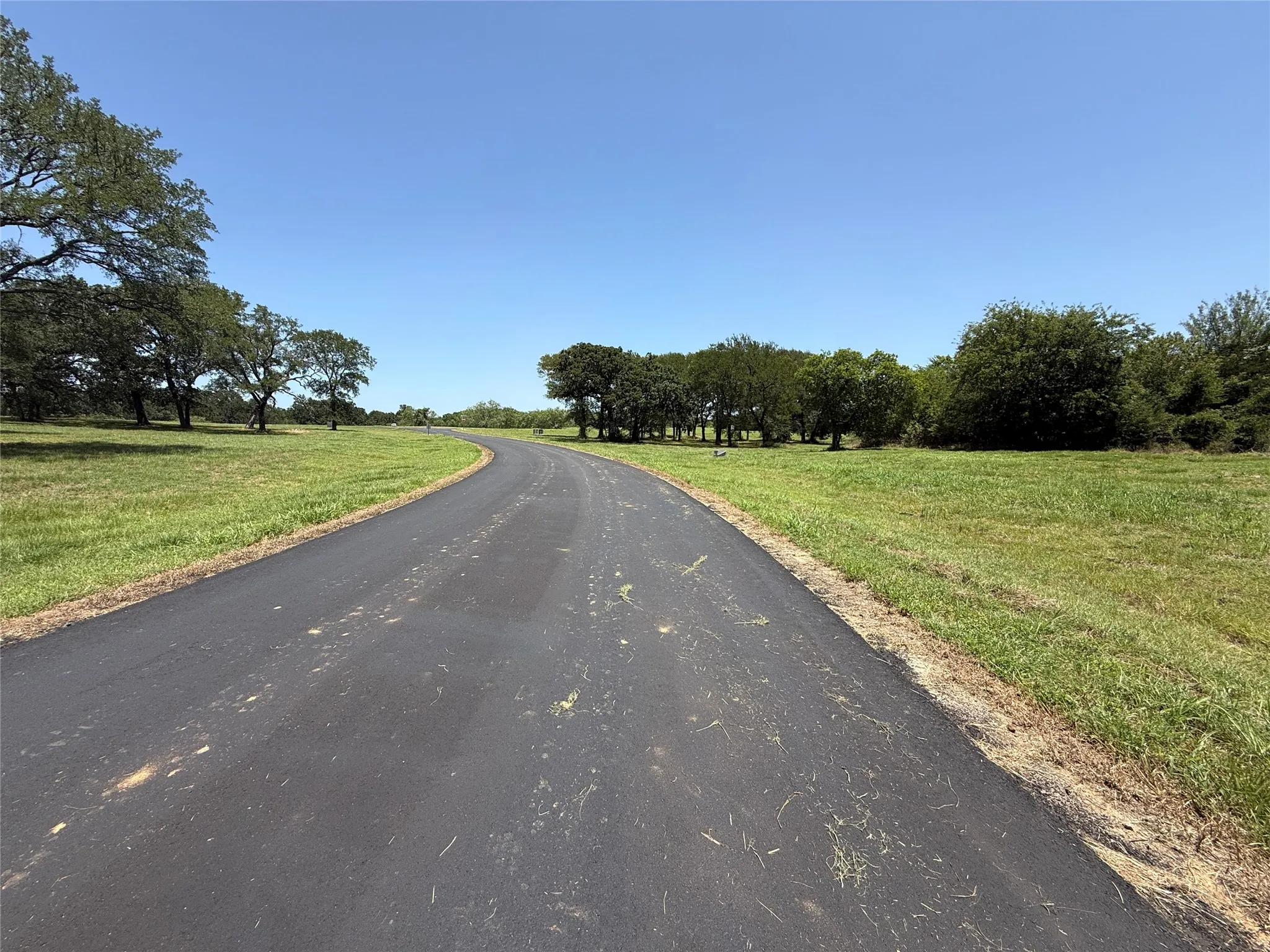 Ground-level view along asphalt road frontage displaying level terrain ready for custom home construction.