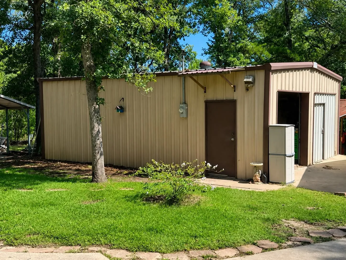 Corrugated metal building featuring a brown door, roll-up garage door, and a covered carport structure