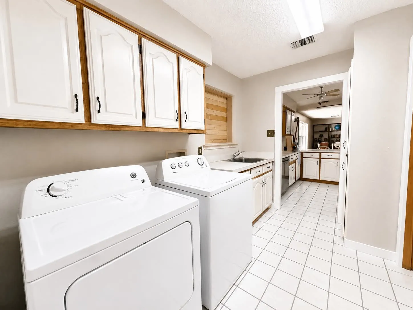 Laundry area featuring white cabinetry with wood trim, a built-in sink, and white square tile flooring