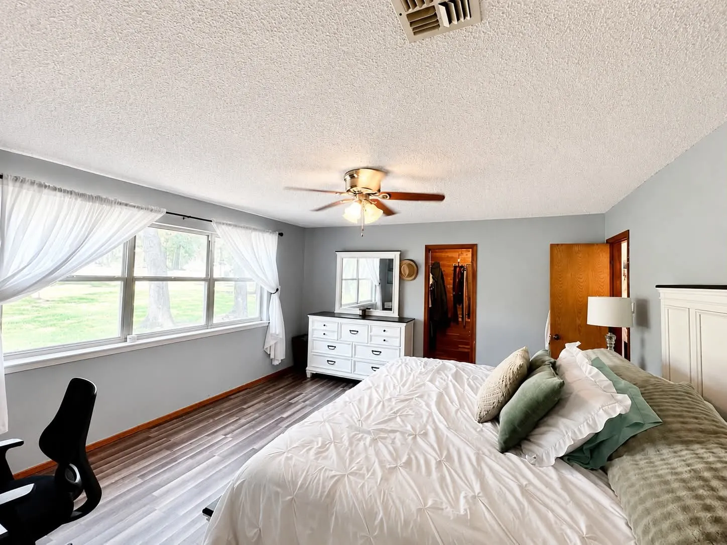 Spacious room featuring wood-finish flooring, a large window with white sheers, and light-colored walls