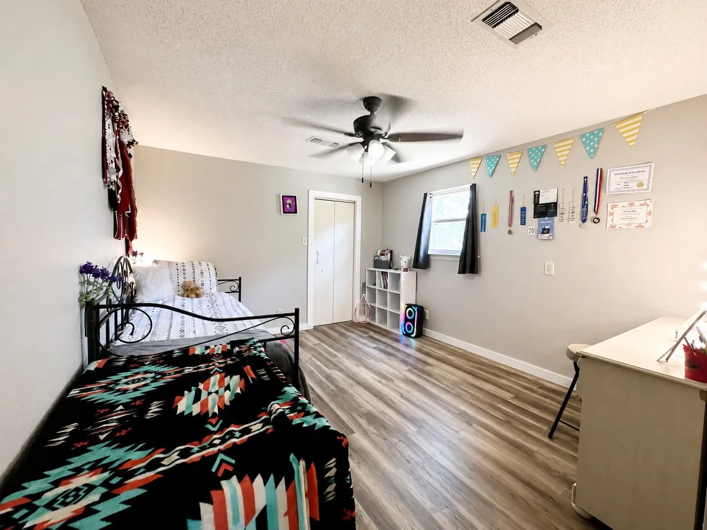 Bright room featuring wood-finish flooring, a ceiling fan with integrated lighting, and a window with dark blinds