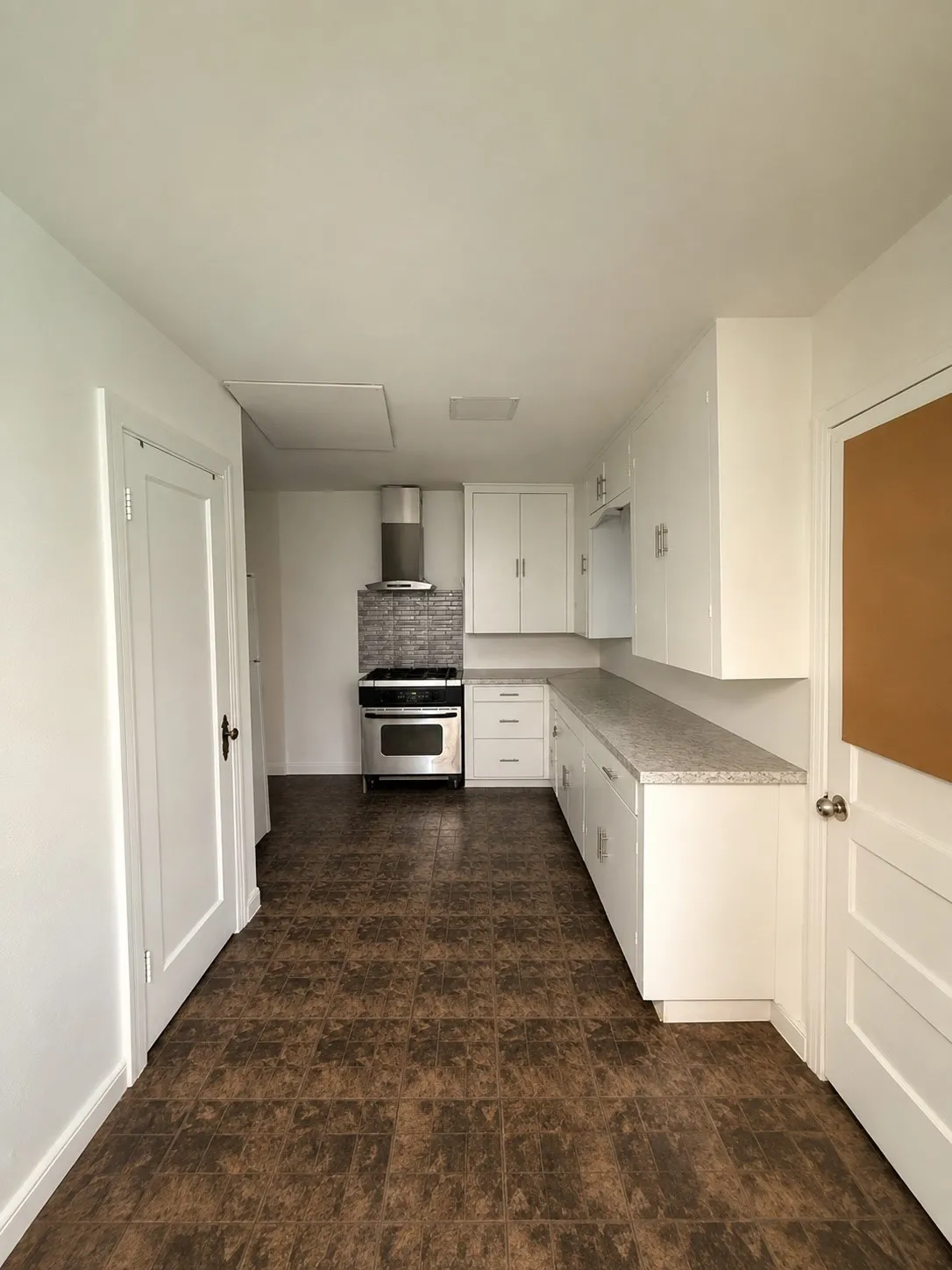 Galley kitchen featuring white cabinetry, light-colored countertops, and stainless steel appliances including a range and range hood