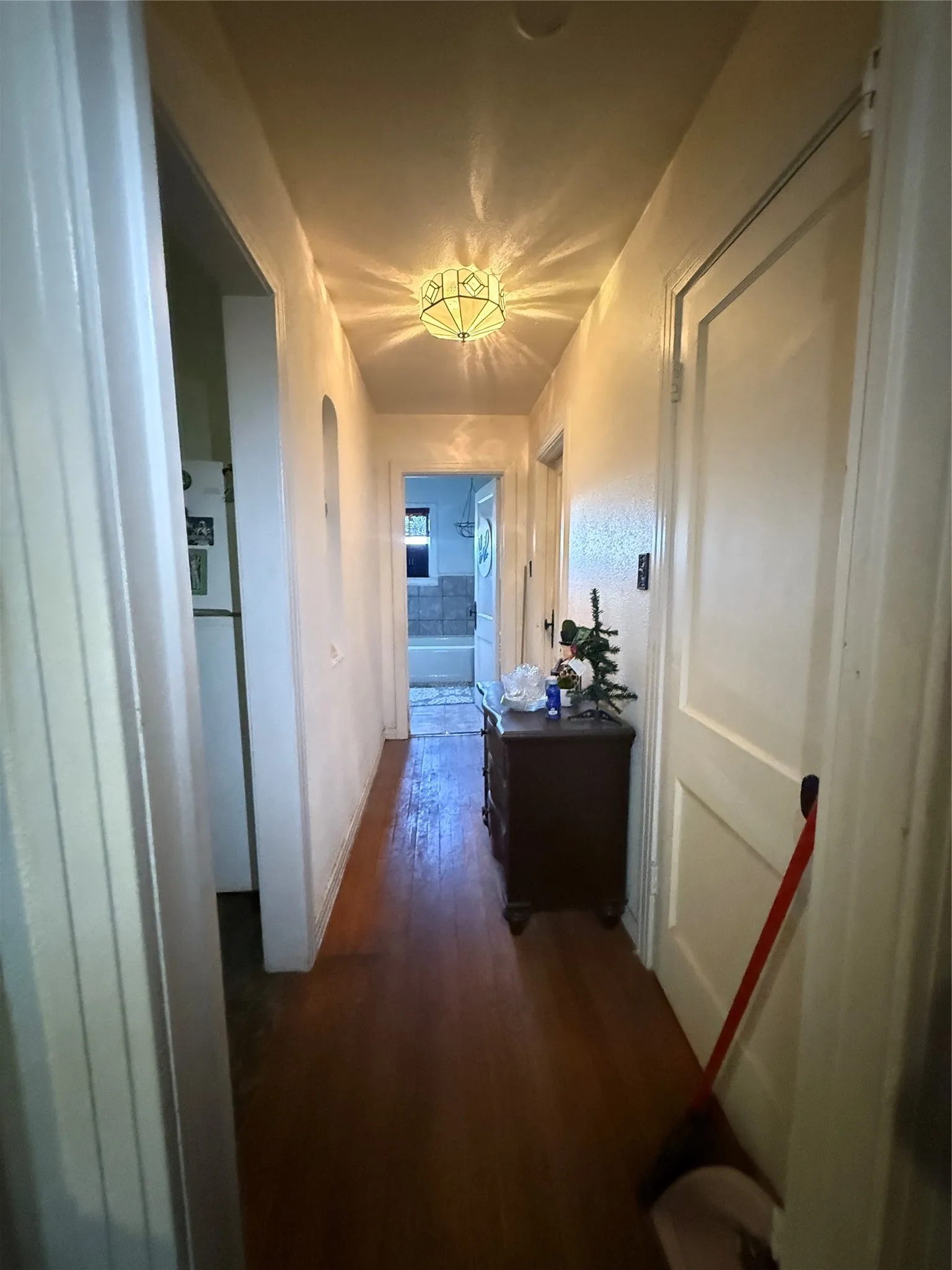 Hallway featuring wood-finish flooring, a decorative ceiling-mounted light fixture, and arched wall openings