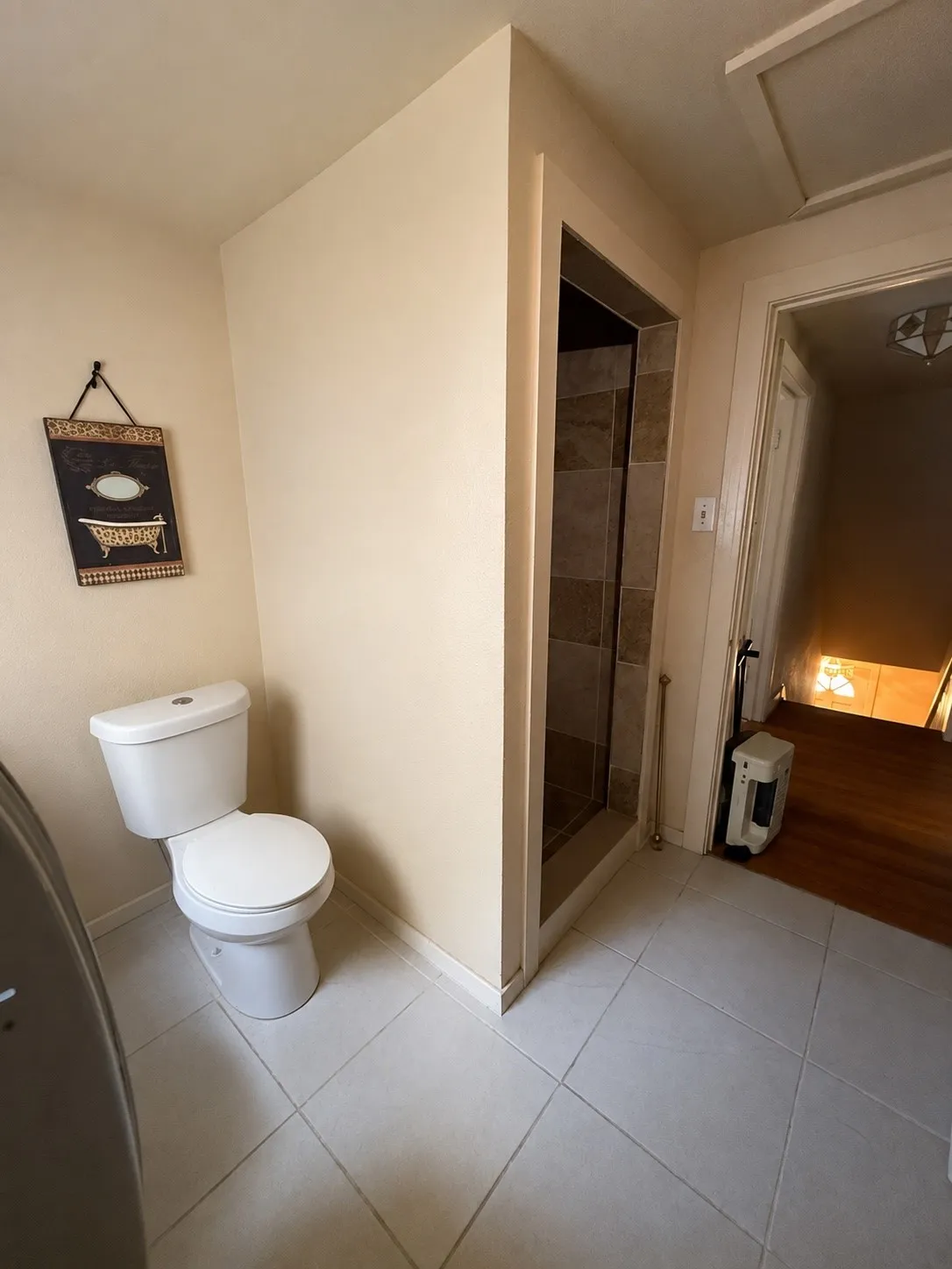 Bathroom featuring a white toilet, tile flooring, and a walk-in shower with stone-look tile surround and glass enclosure
