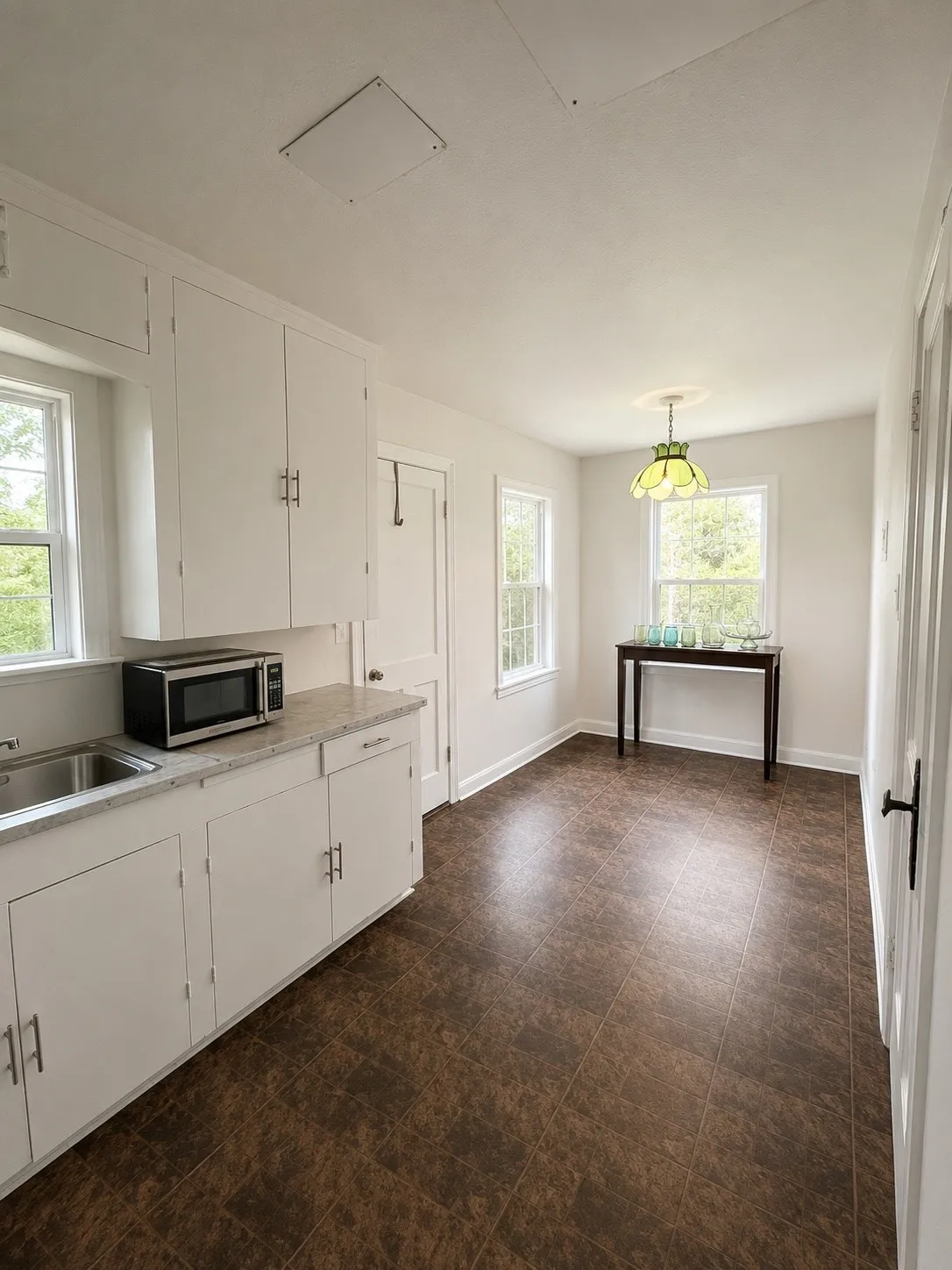 Bright kitchen and dining area featuring white cabinetry, a stainless steel sink, light-toned countertops, and large windows providing abundant natural light