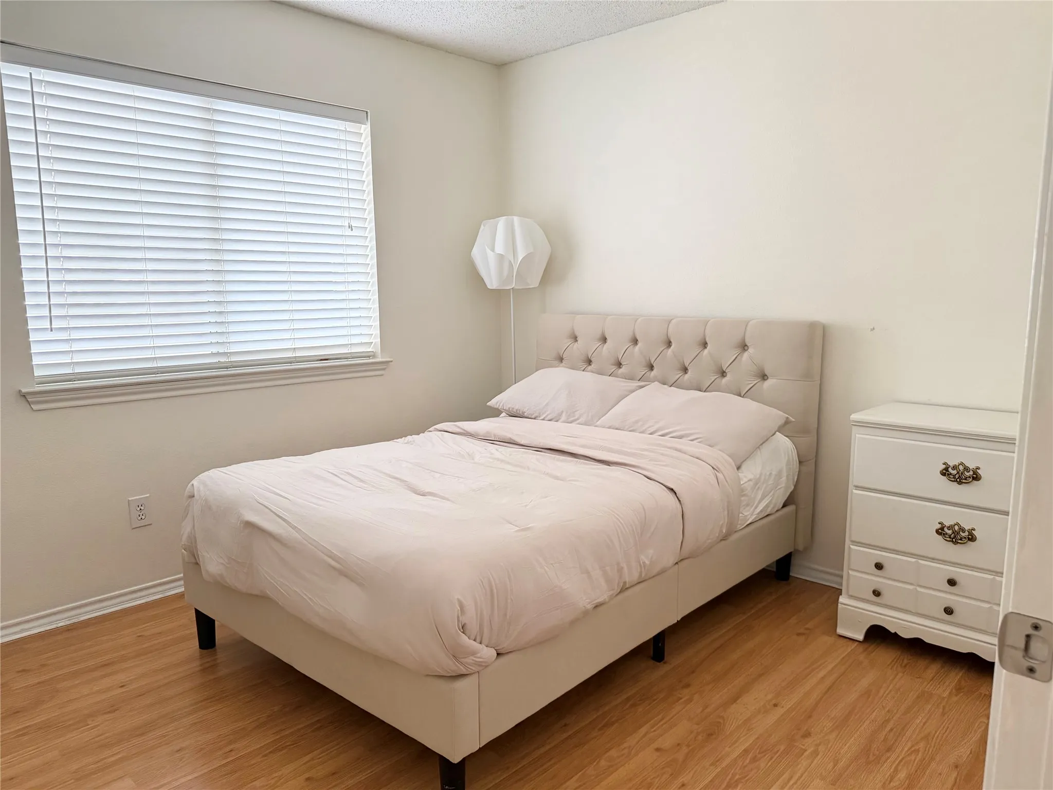 Room with wood-finish flooring, a window with blinds, and light-toned walls