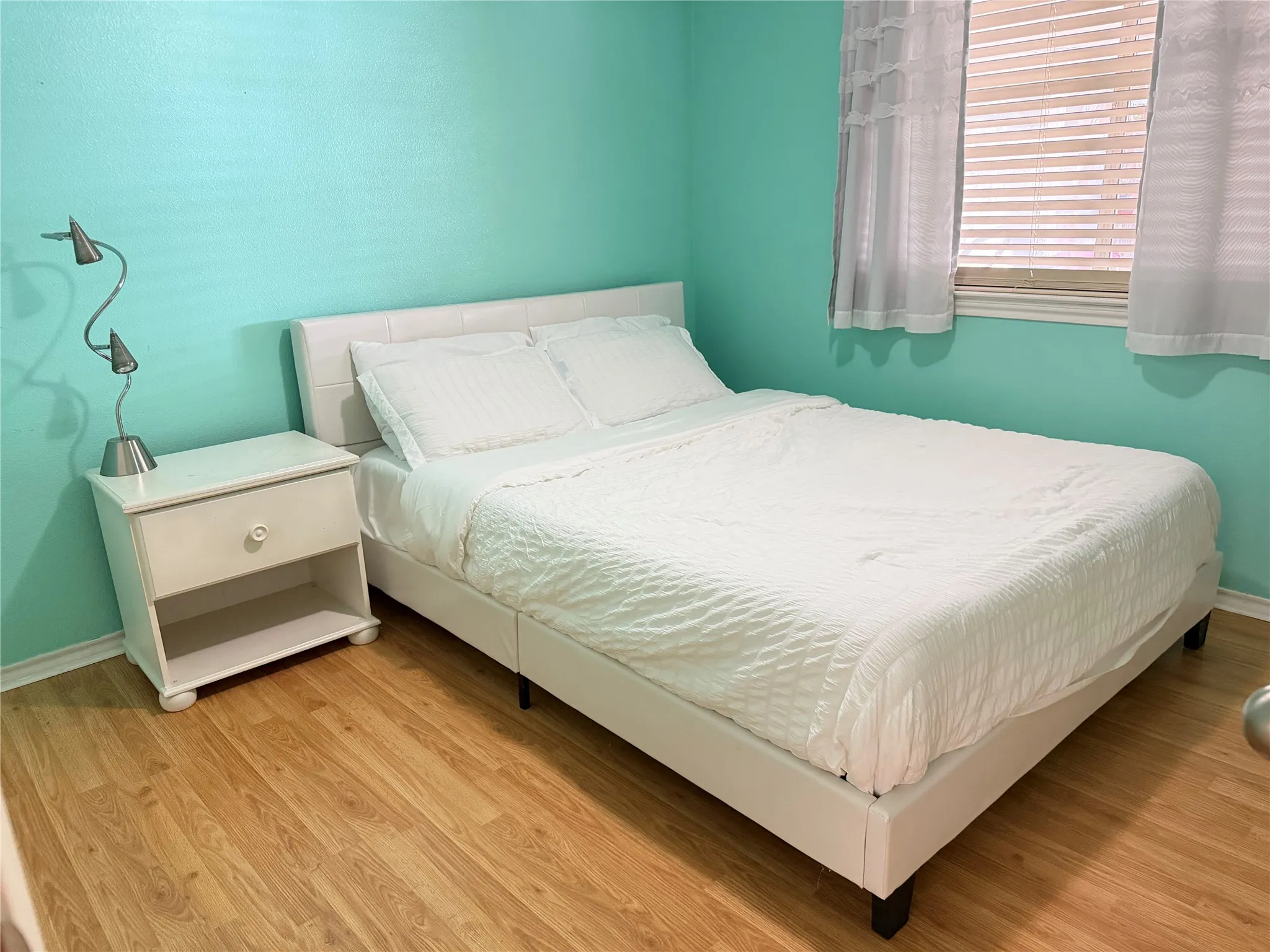 Bedroom featuring light wood-finish flooring, a window with horizontal blinds, and a light blue wall color