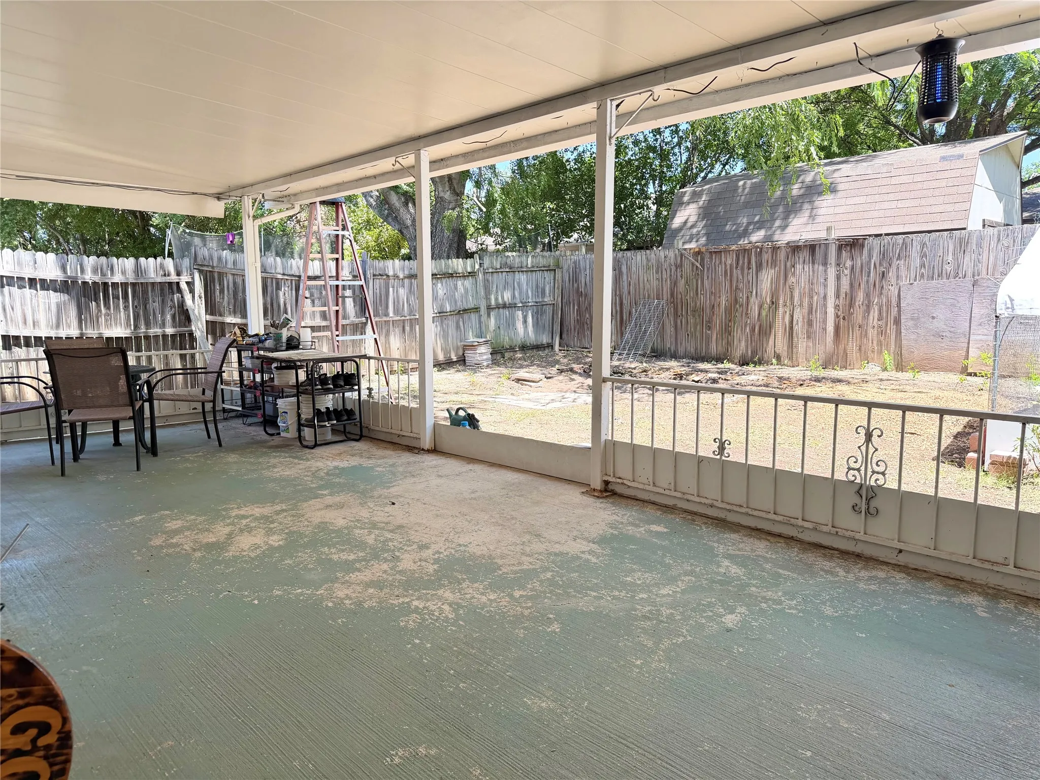 Covered patio with a concrete surface, featuring a metal railing and a wood privacy fence defining the property perimeter